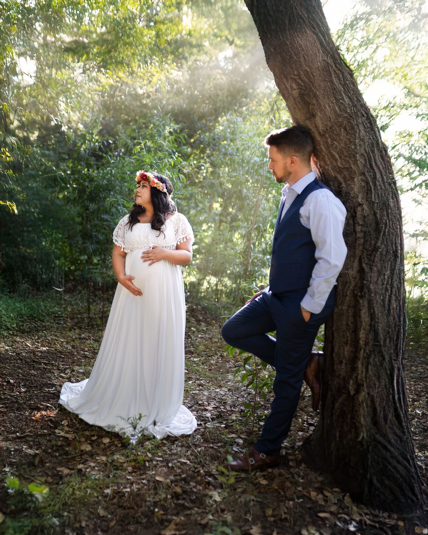 A couple shares intimate moments in a wooded setting with sunlight filtering through the trees during a romantic photoshoot.