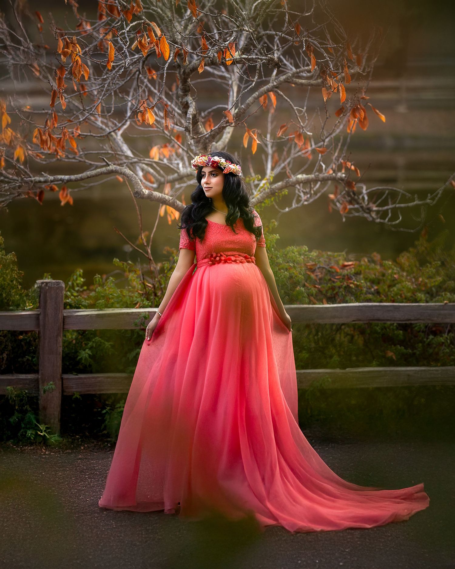 A flowing coral pink tulle gown creates a dreamy silhouette against an autumn backdrop with bare branches.