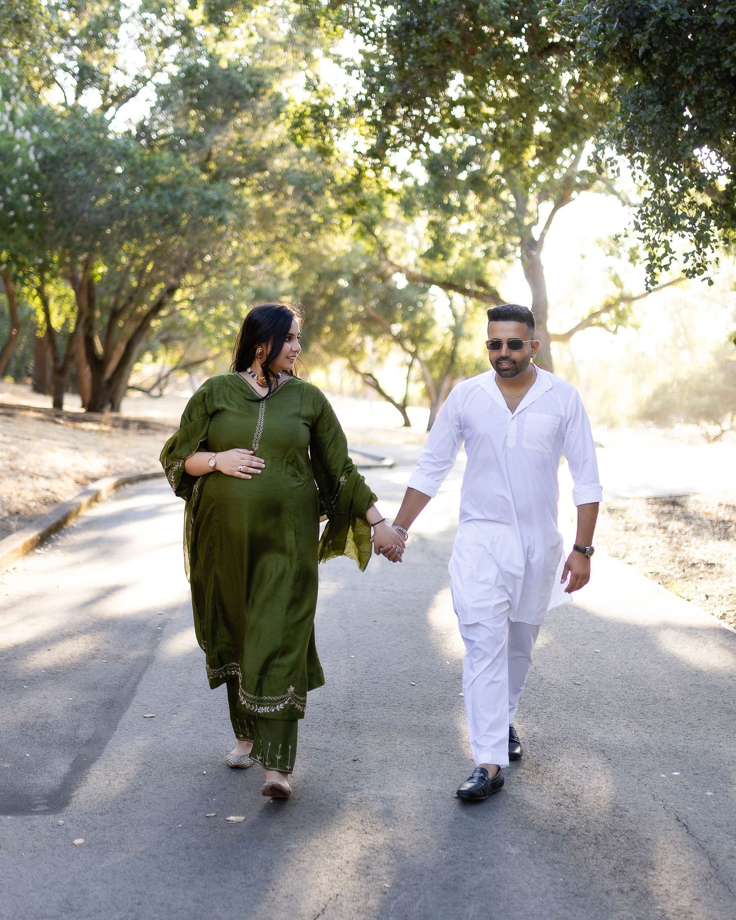 Two people walking together on a tree-lined path, one wearing green and one in white clothing.