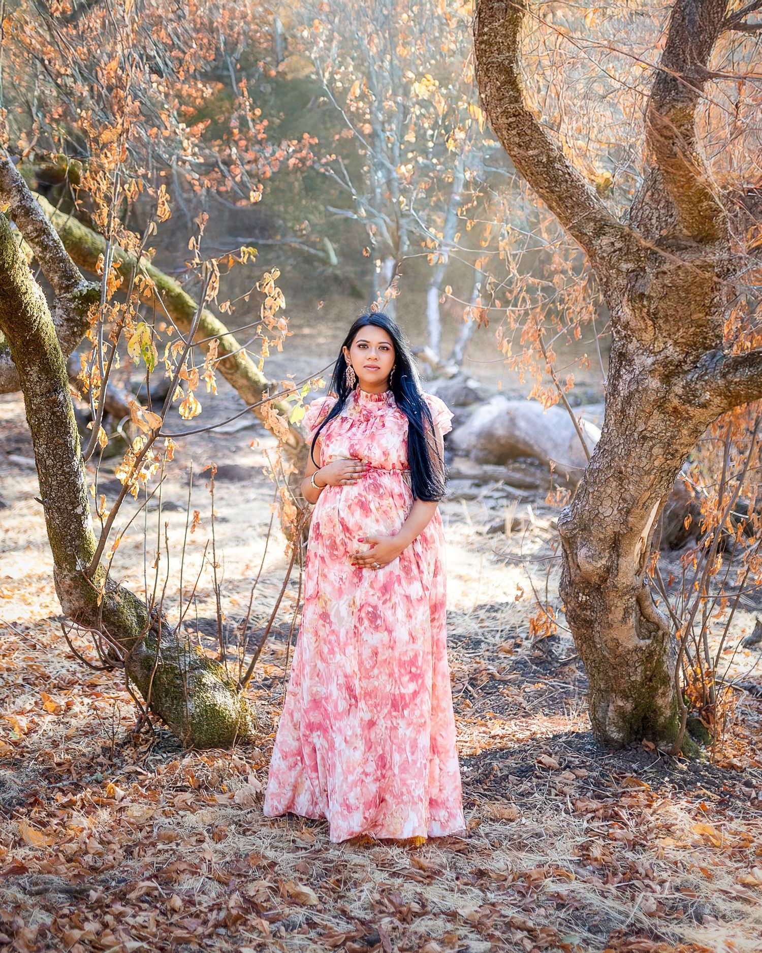 A dreamy autumn scene with a pink floral dress contrasting against fallen leaves and misty woodland trees in the background.