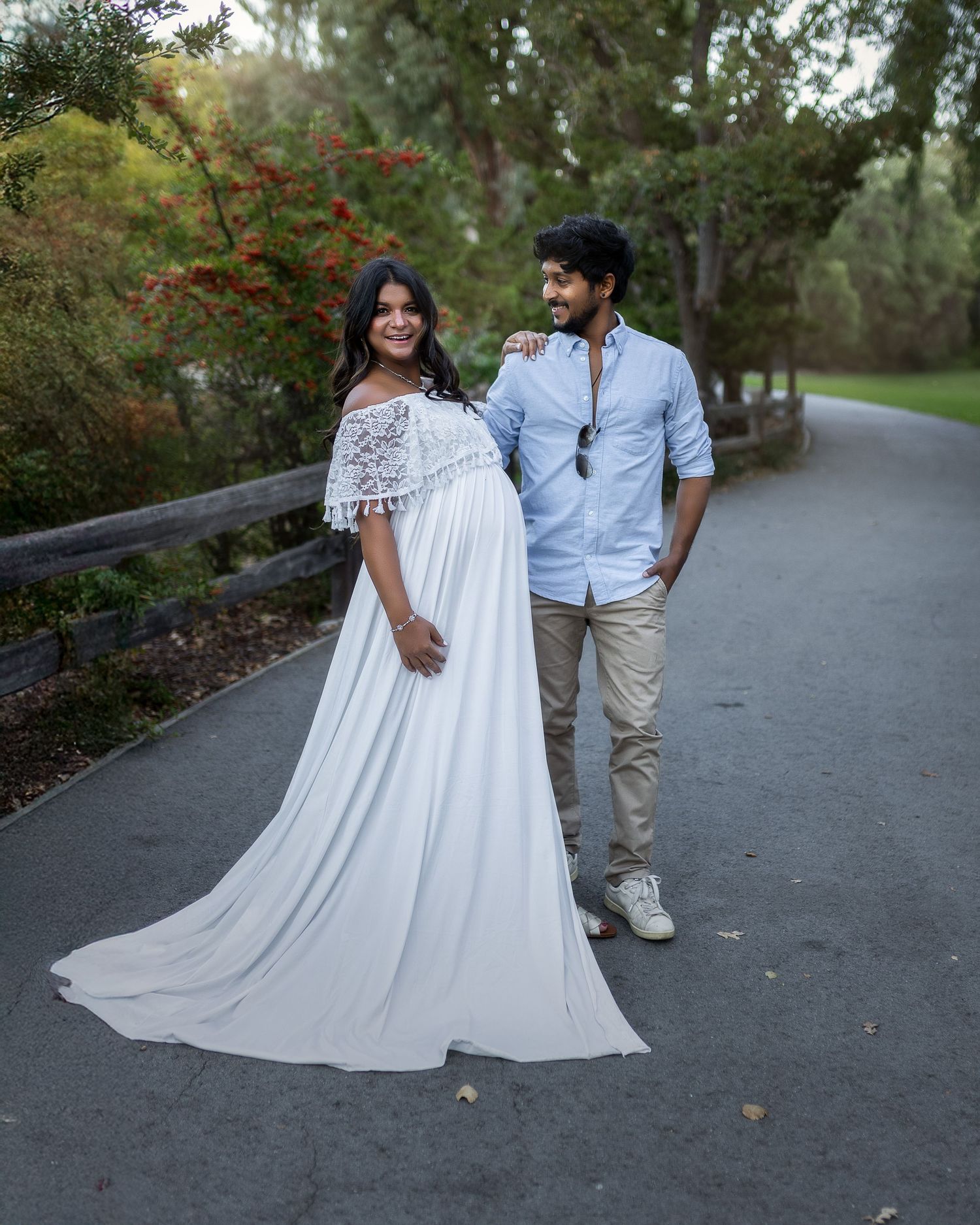 A couple in white dress and blue shirt walking together on a paved path surrounded by lush greenery.