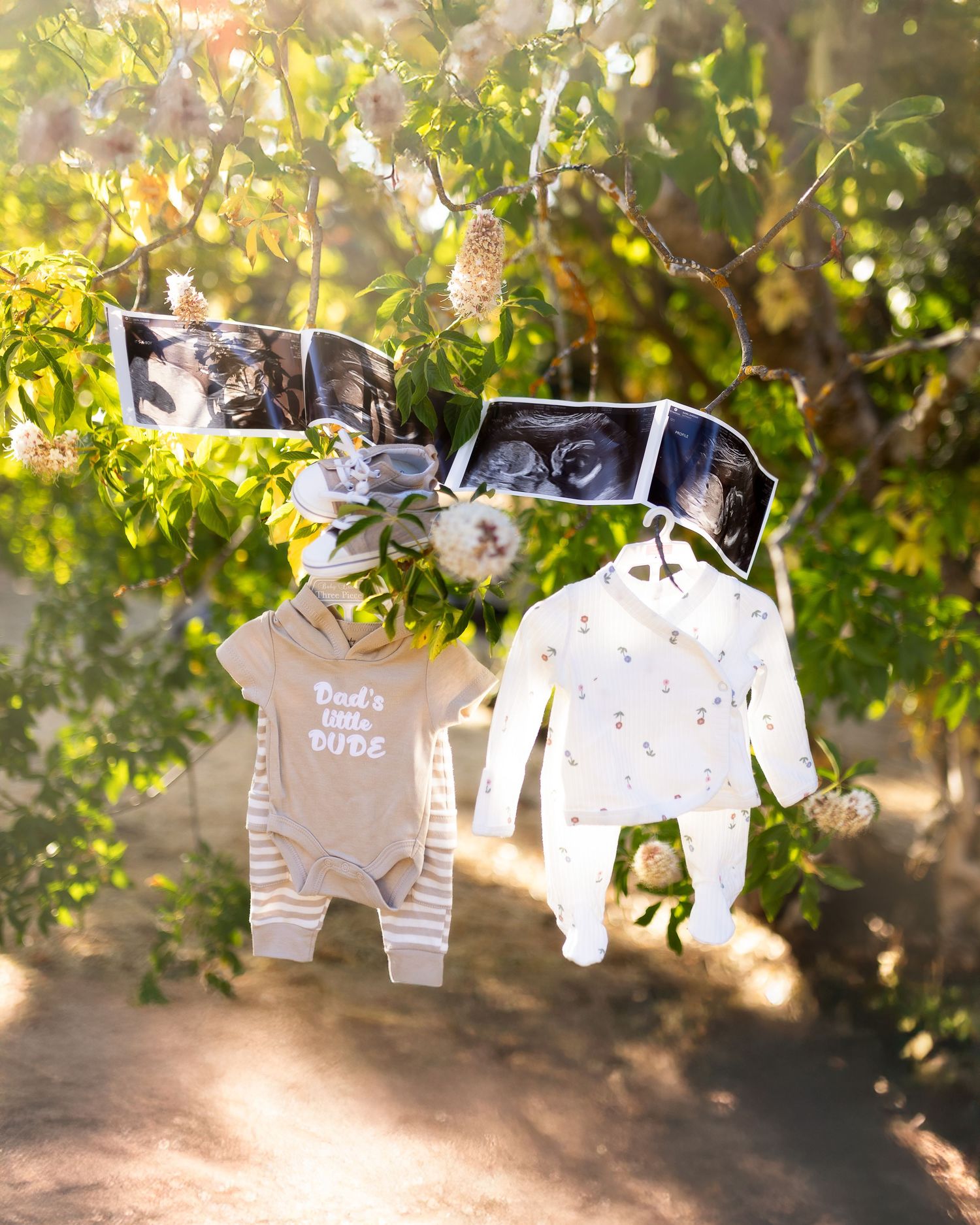 Baby clothes and onesies hanging on a clothesline against a sunlit garden background with green foliage.