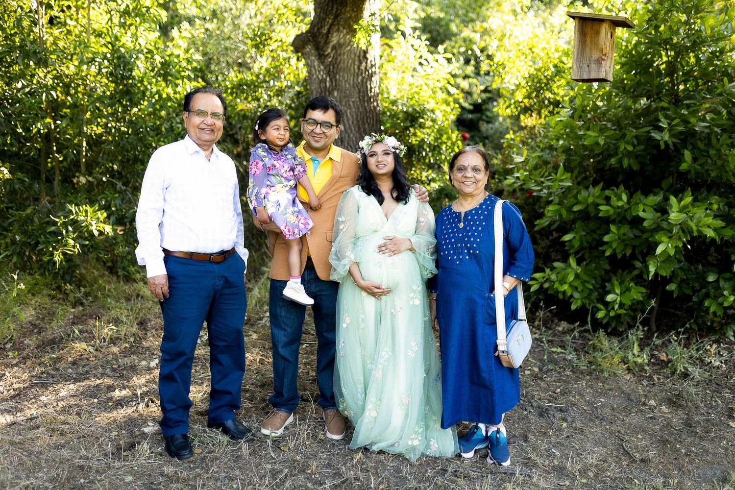 A group stands together outdoors on a wooded path wearing formal attire in blue and mint green colors.