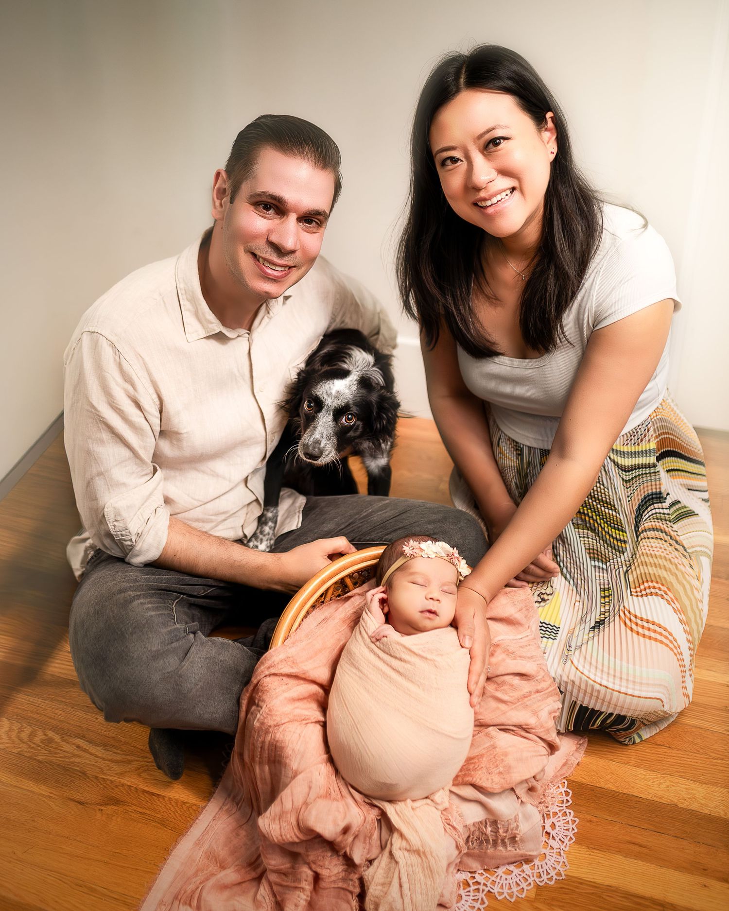 Family sitting on wooden floor with their dog in casual home setting with warm lighting.