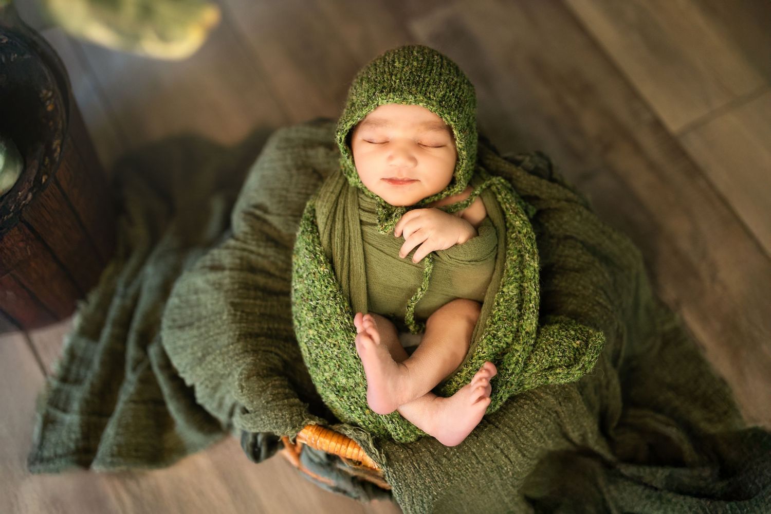 Newborn baby swaddled in soft green knitted blanket during professional photo session.