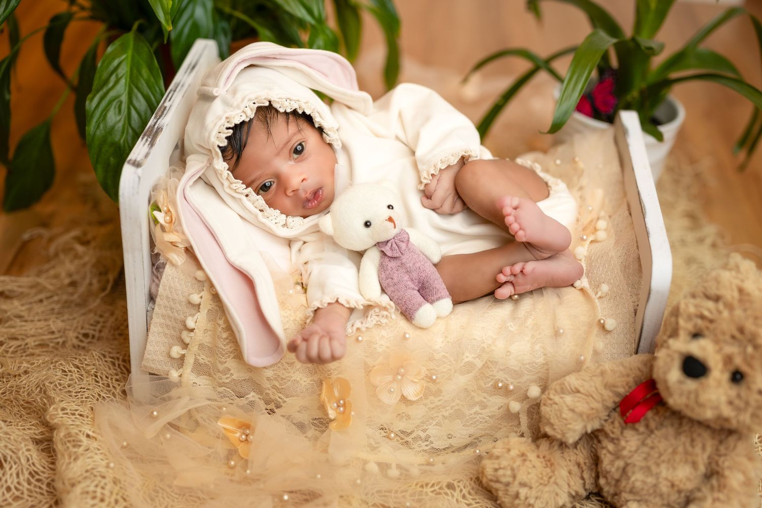 A newborn baby lies peacefully in a cream-colored basket surrounded by soft fabrics and plush toys.