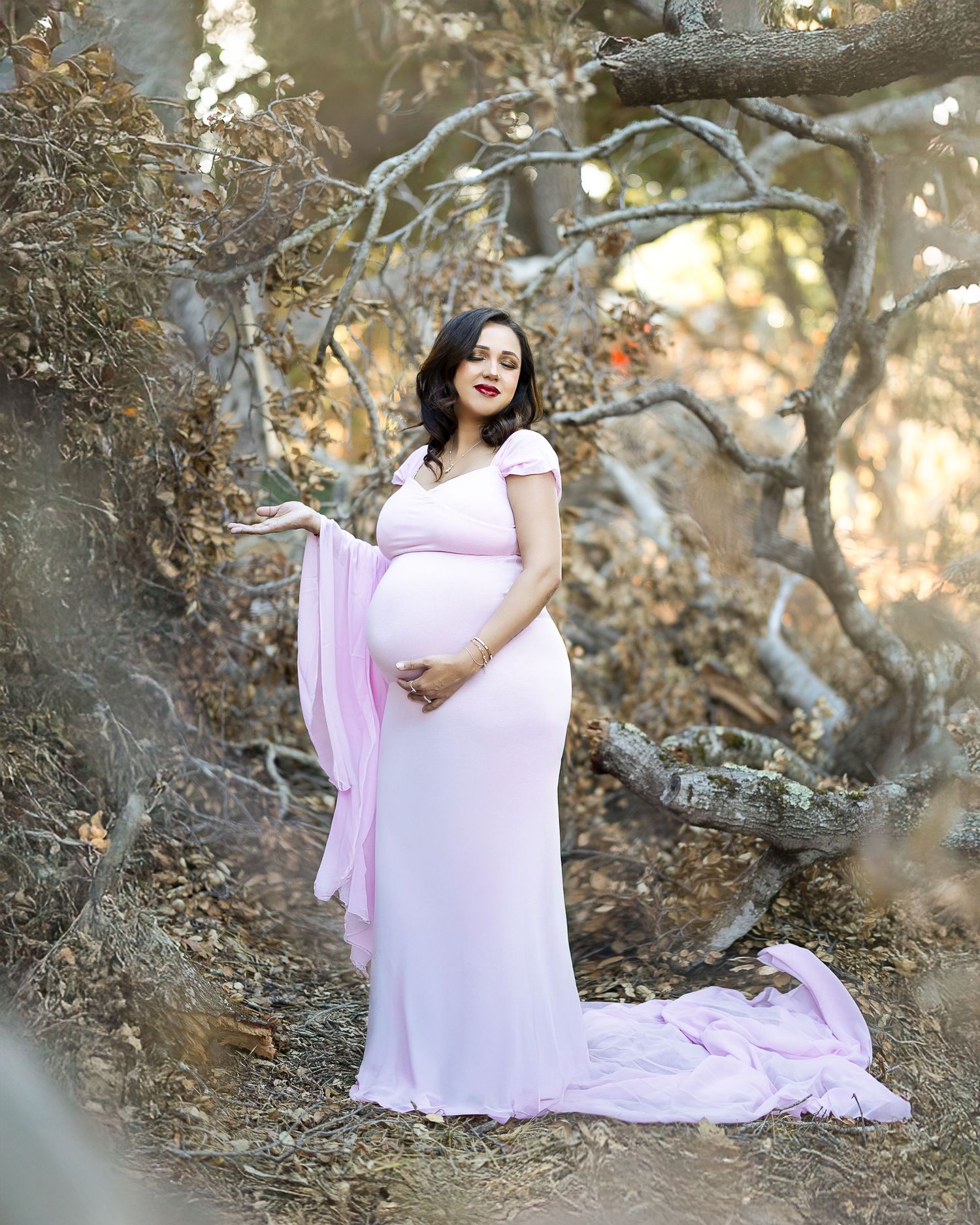 A flowing lavender dress creates an ethereal maternity portrait against a natural outdoor setting with golden sunlight.