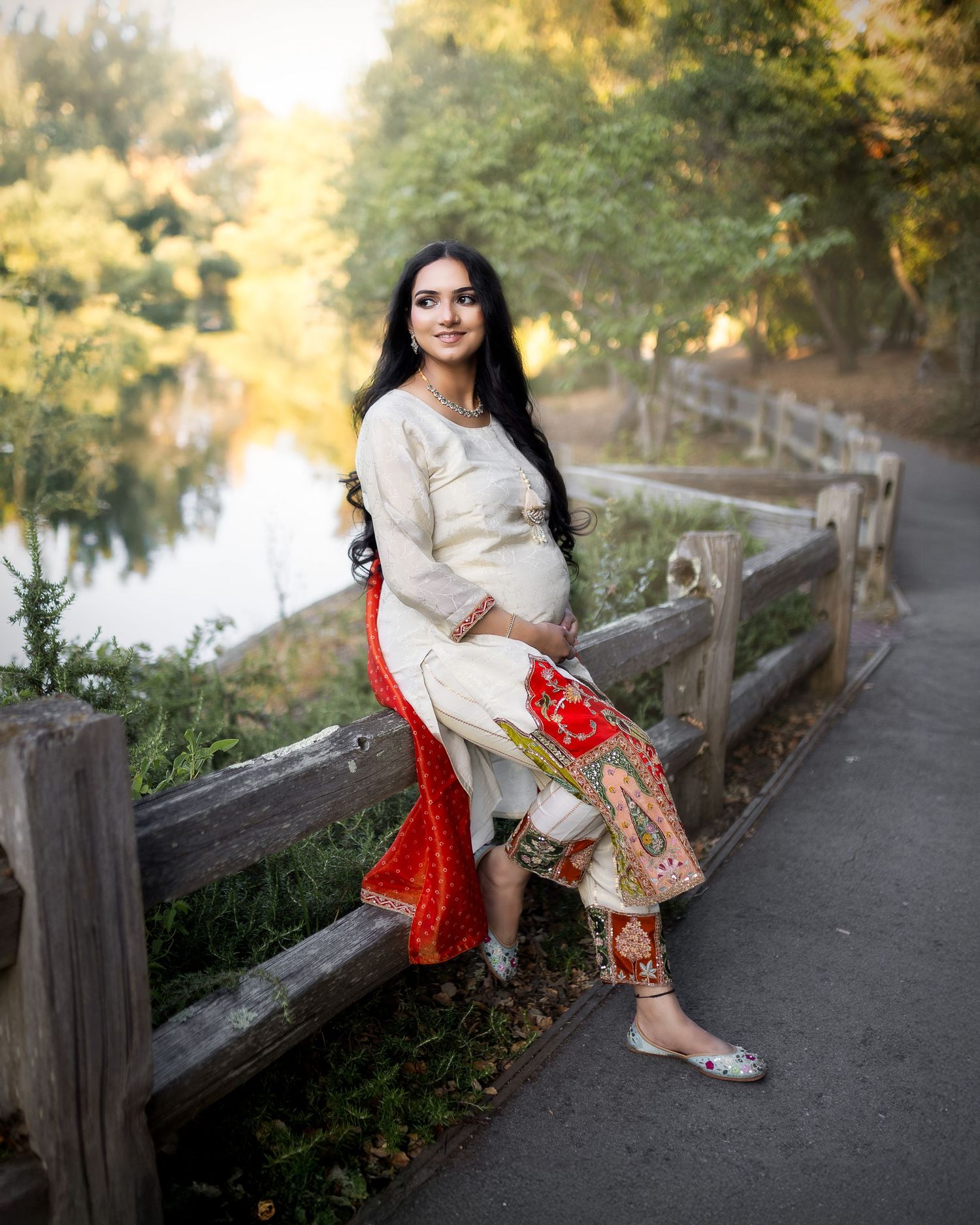 Traditional Indian attire in cream and red colors photographed in an autumn park setting with wooden railings and foliage.