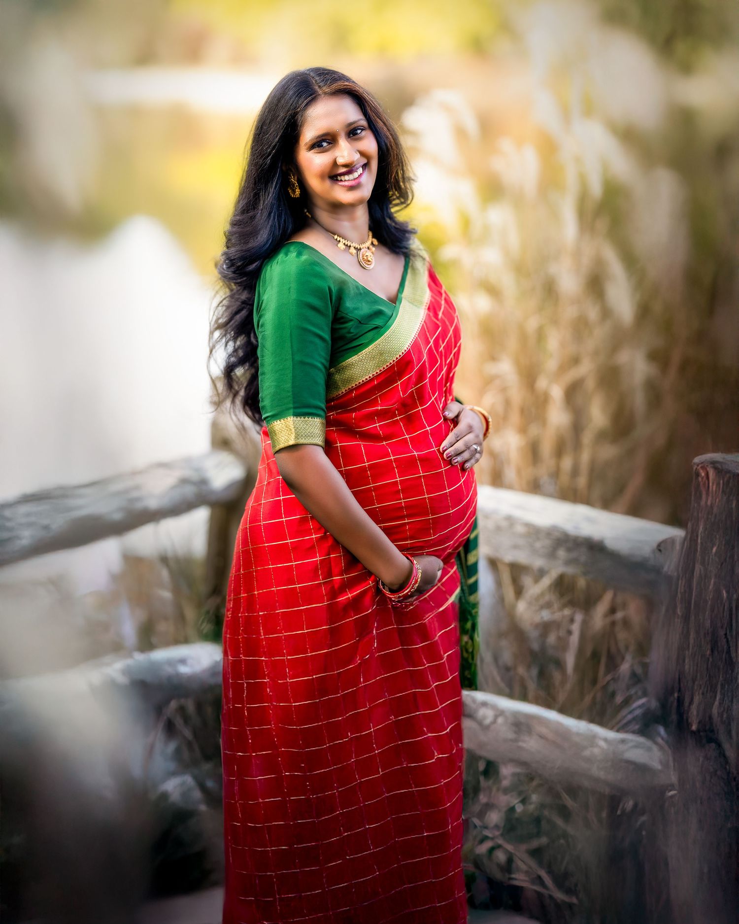 Beautiful traditional red and green saree with gold border worn in an outdoor setting with soft bokeh background.