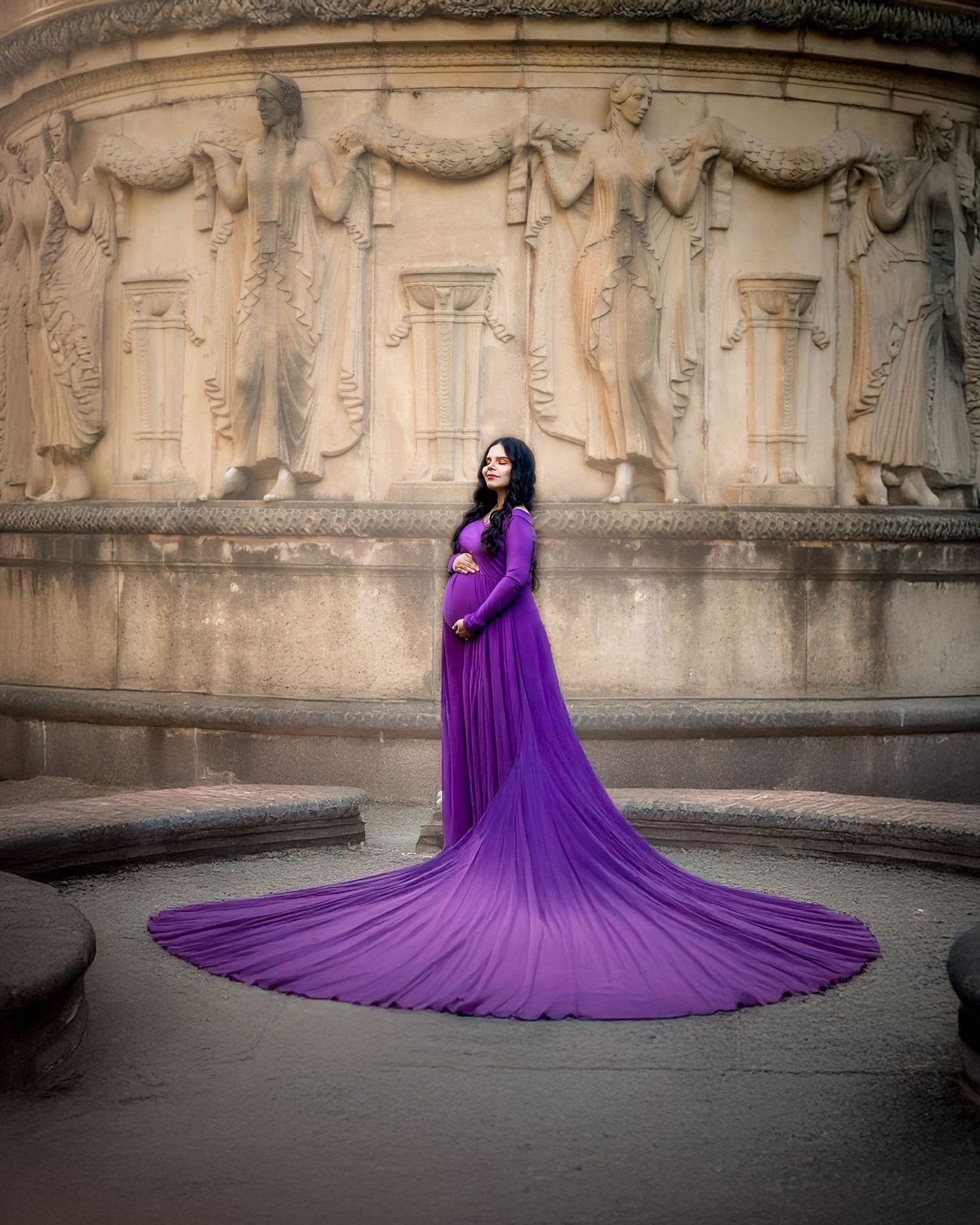 A flowing purple maternity gown with long train photographed against ornate stone architectural details.