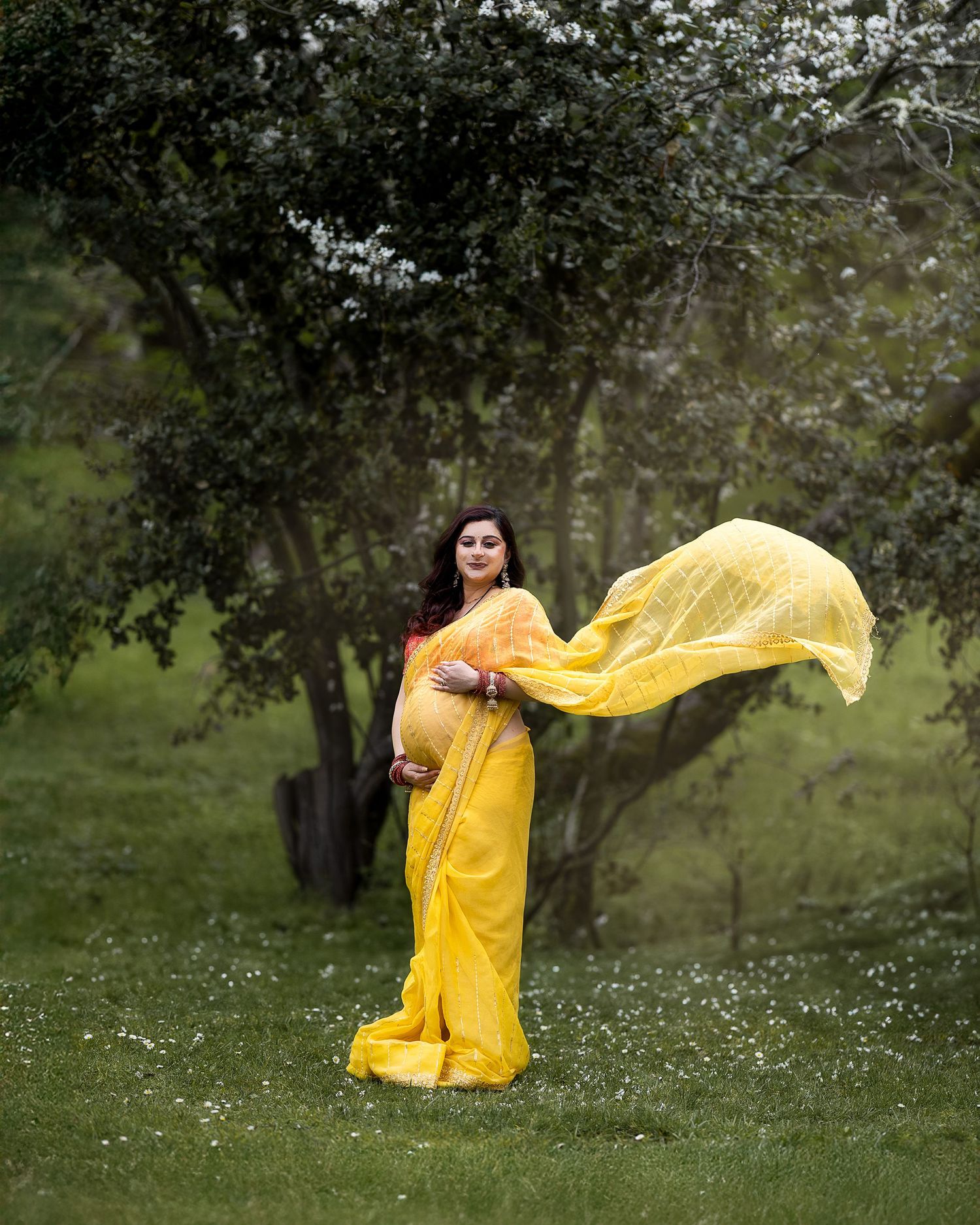 A flowing yellow dress creates movement in an outdoor garden setting with white flowers and green foliage.