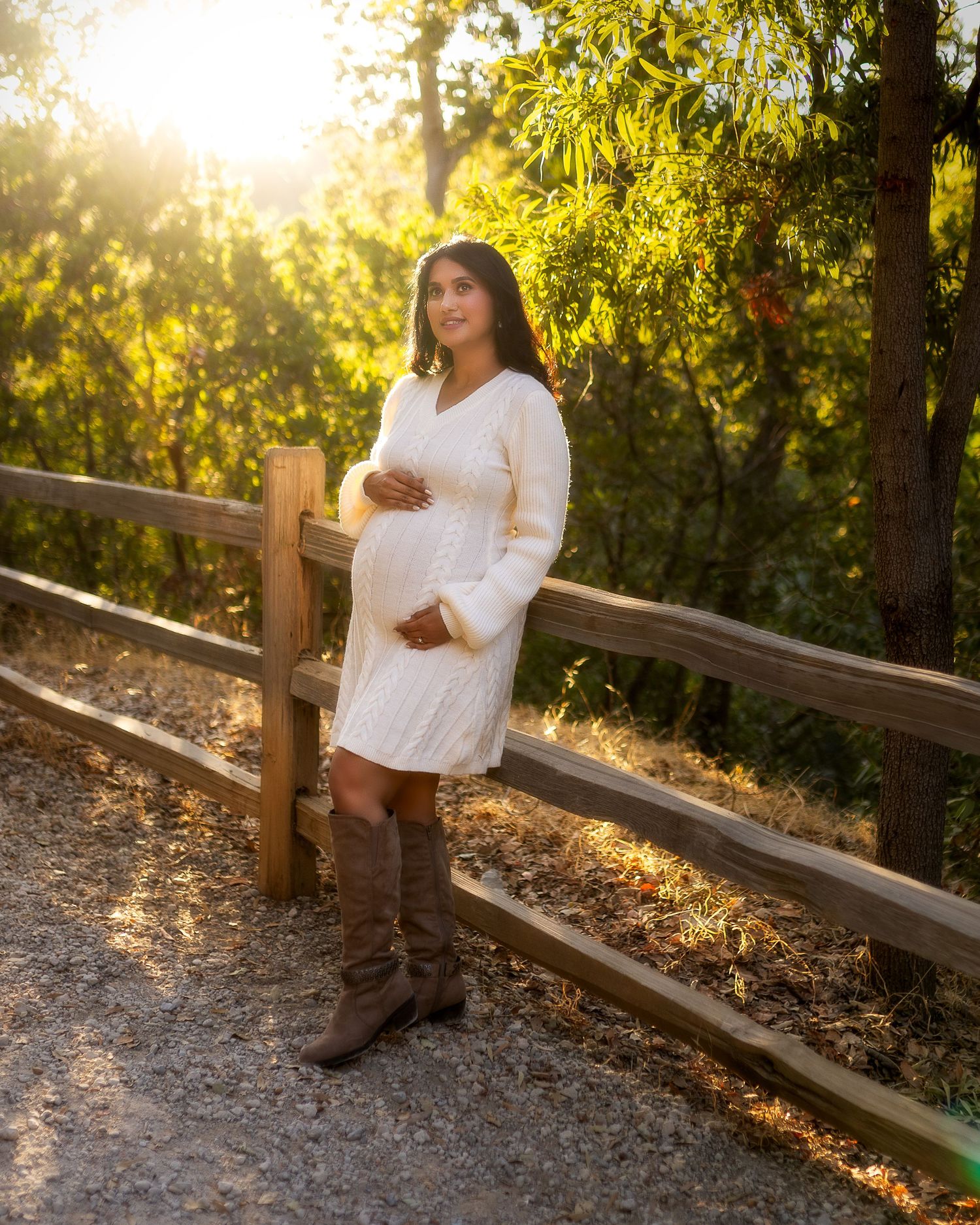 A figure stands against a rustic wooden fence at golden hour with sunlit trees creating a warm, glowing backdrop.