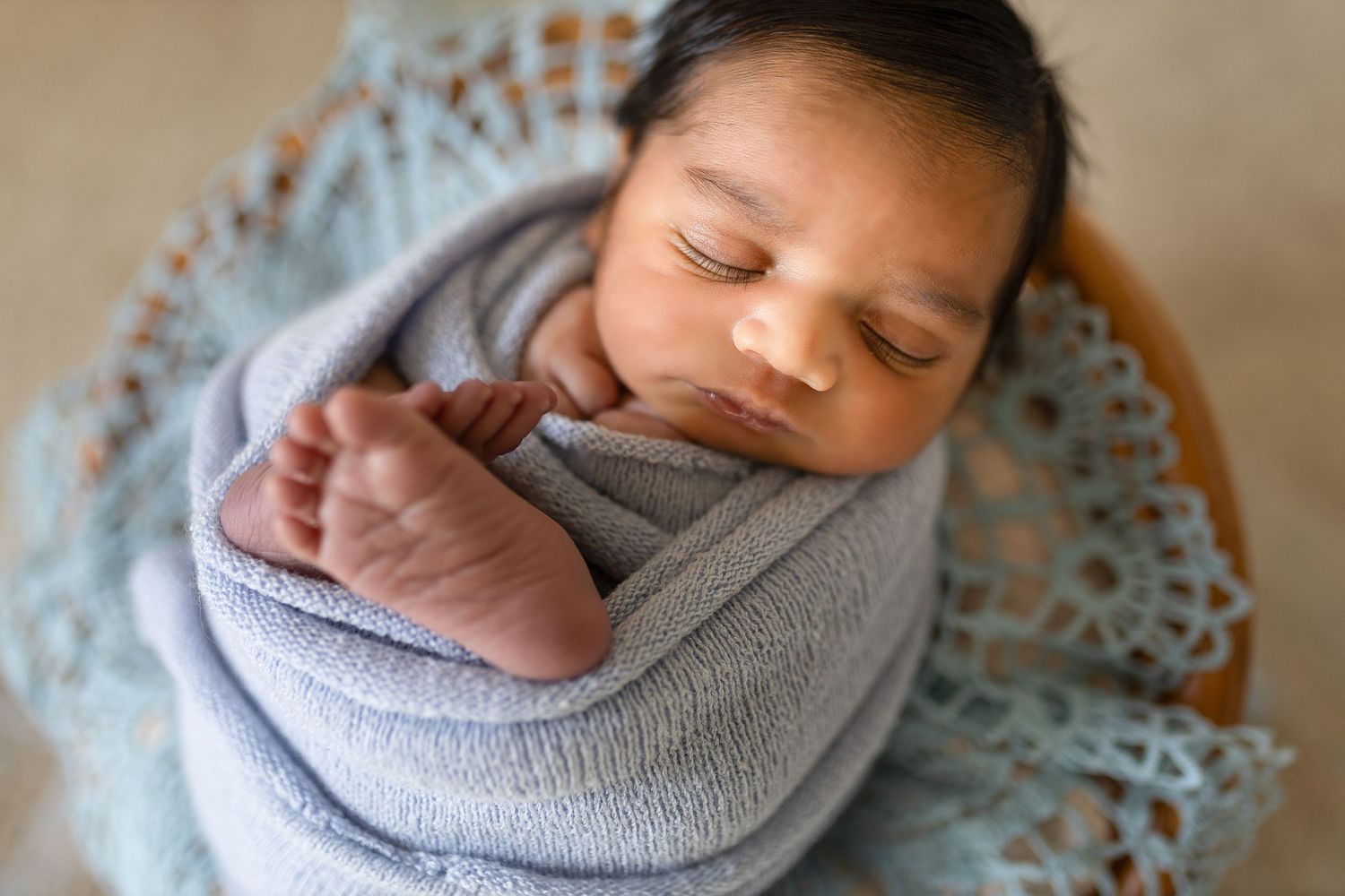Peaceful sleeping newborn wrapped in soft gray swaddle blanket resting on delicate lace fabric.