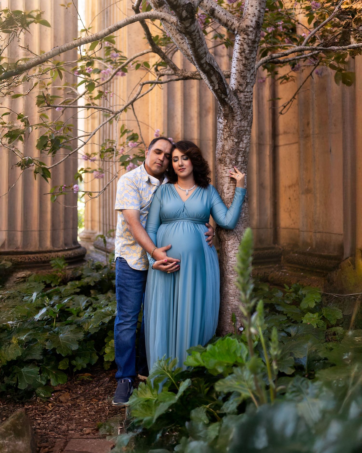 A couple shares an intimate moment against a wooden fence in a garden setting with soft golden lighting.