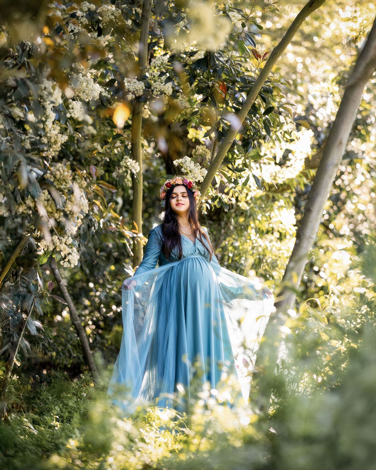 A dreamy portrait series in a garden setting with flowing blue dress and floral surroundings in golden light.
