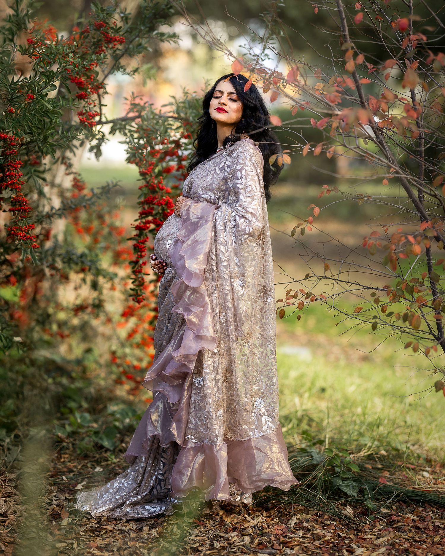 A figure in a lavender gown poses gracefully among autumn branches with red berries in a dreamy outdoor setting.