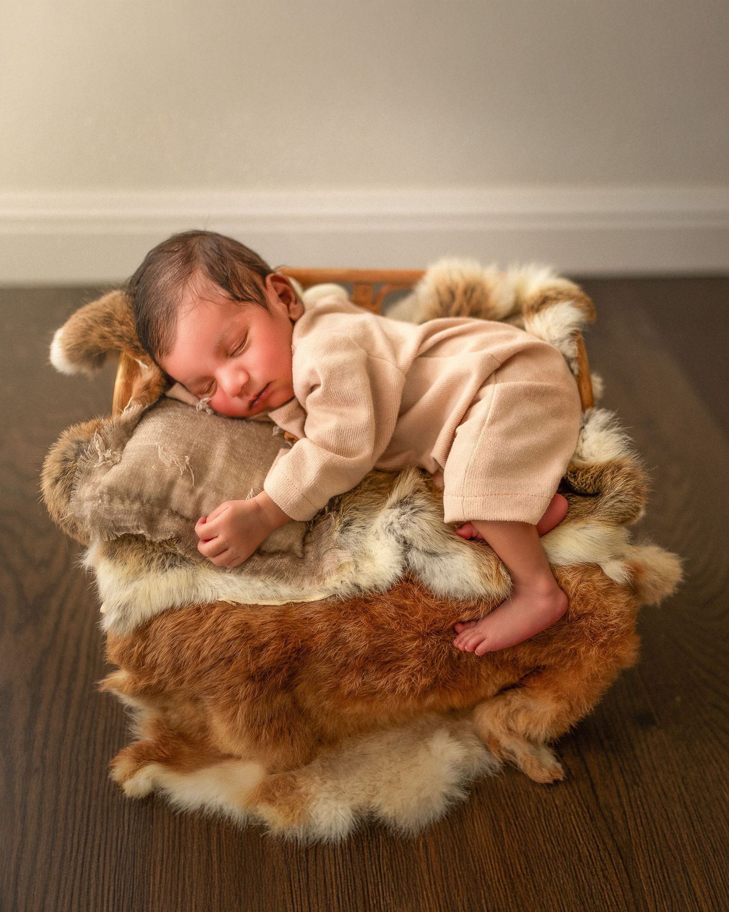 A sleeping infant rests on a fluffy brown fur rug on a wooden floor.