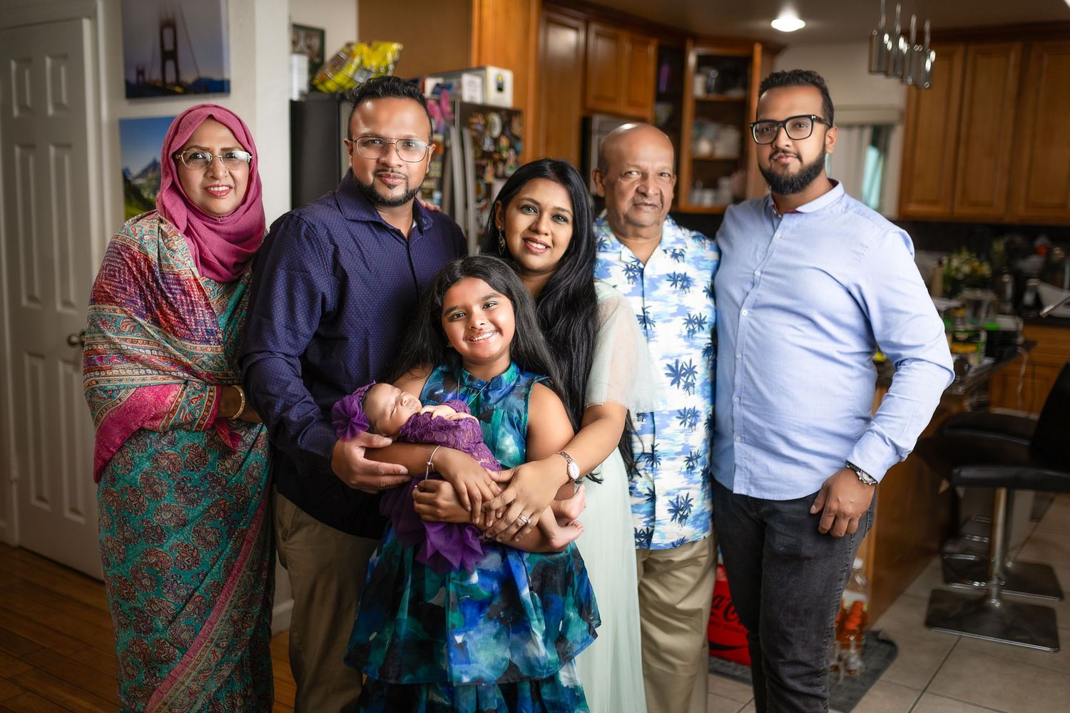 A multigenerational family poses together in their kitchen for a warm group portrait.