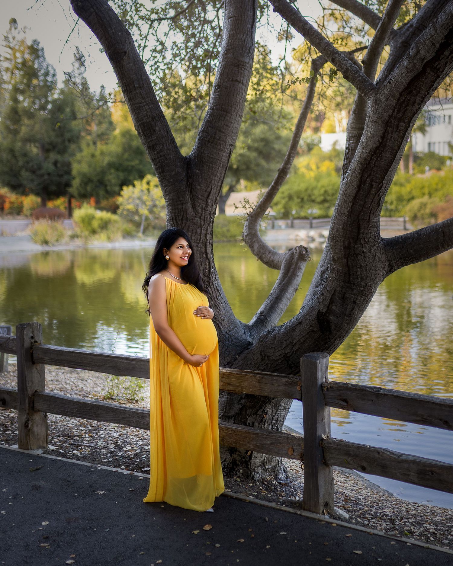A person in a flowing yellow dress poses gracefully near a lake with trees creating a natural frame around them.