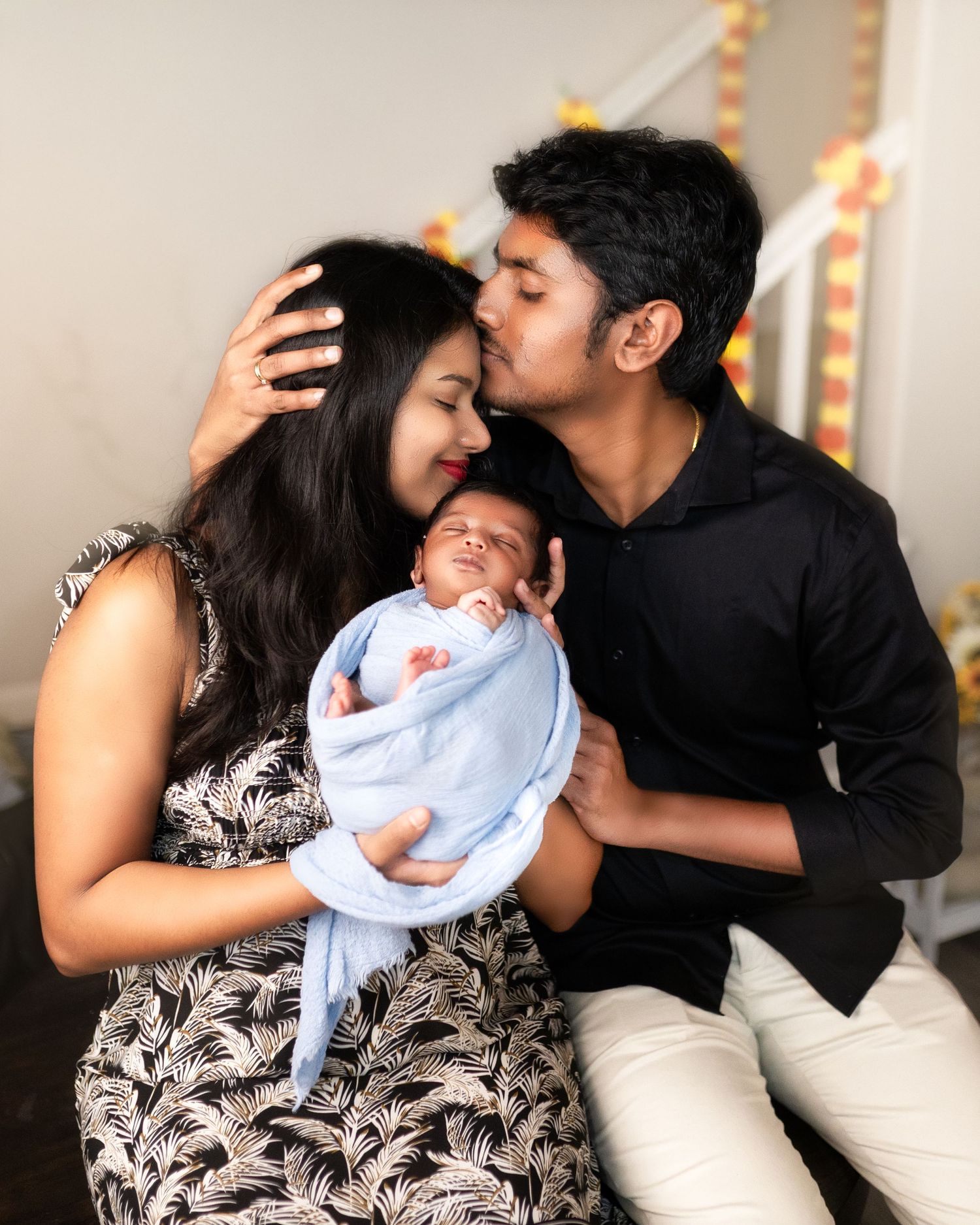 A family shares tender moments together while holding their newborn baby wrapped in a light blue blanket.