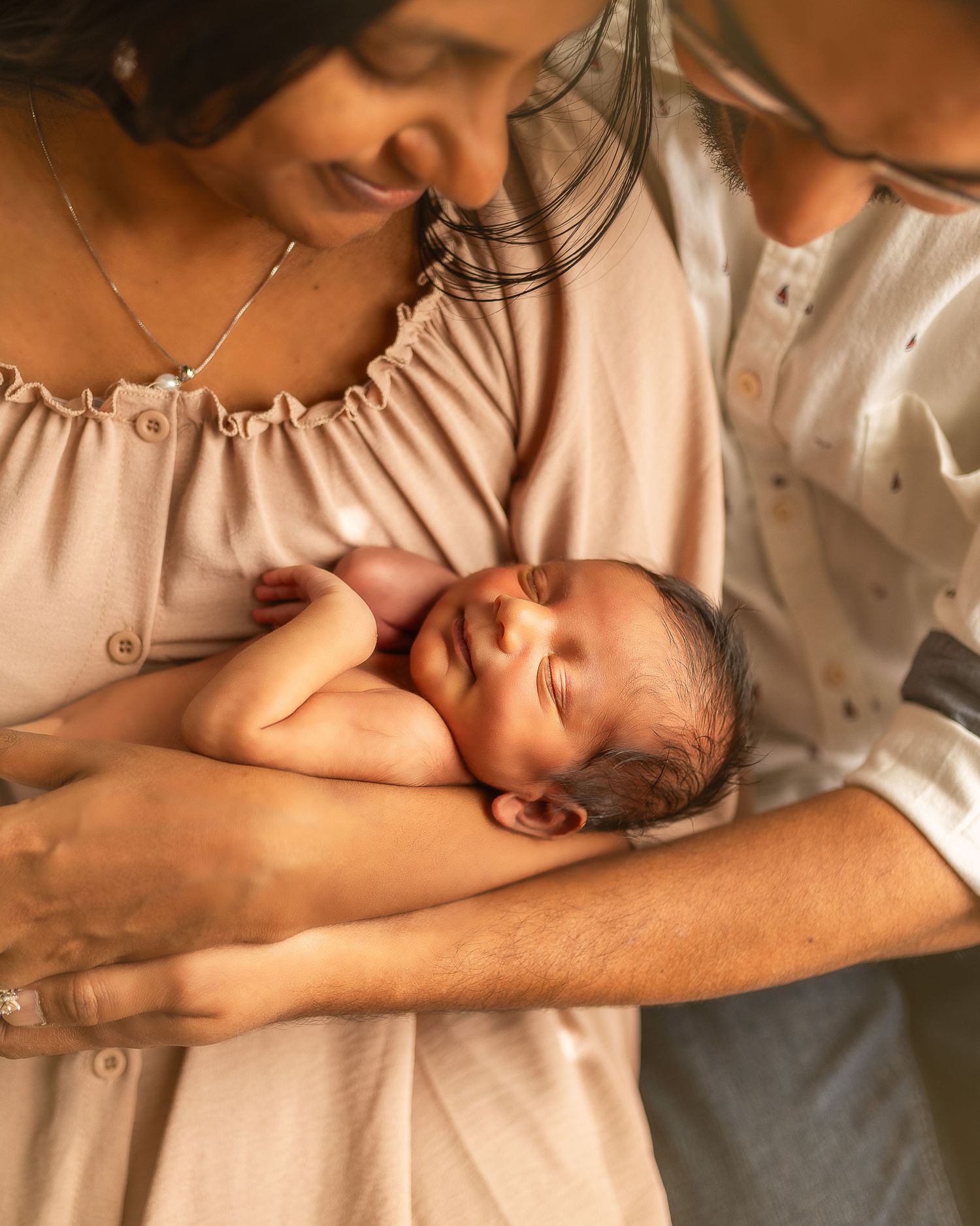 A tender moment of breastfeeding captured in warm tones as a parent nurtures their newborn in a cream-colored setting.