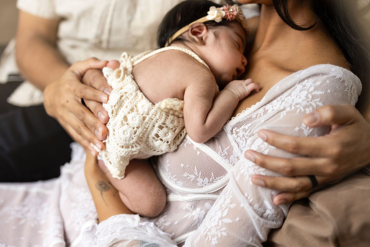 A tender moment captured in soft white lace as a baby is cradled in loving arms during an intimate portrait session.