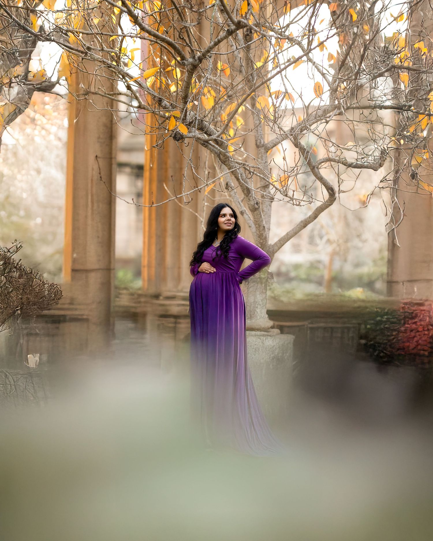 A person in a flowing purple gown poses gracefully among autumn trees in a dreamy outdoor portrait session.