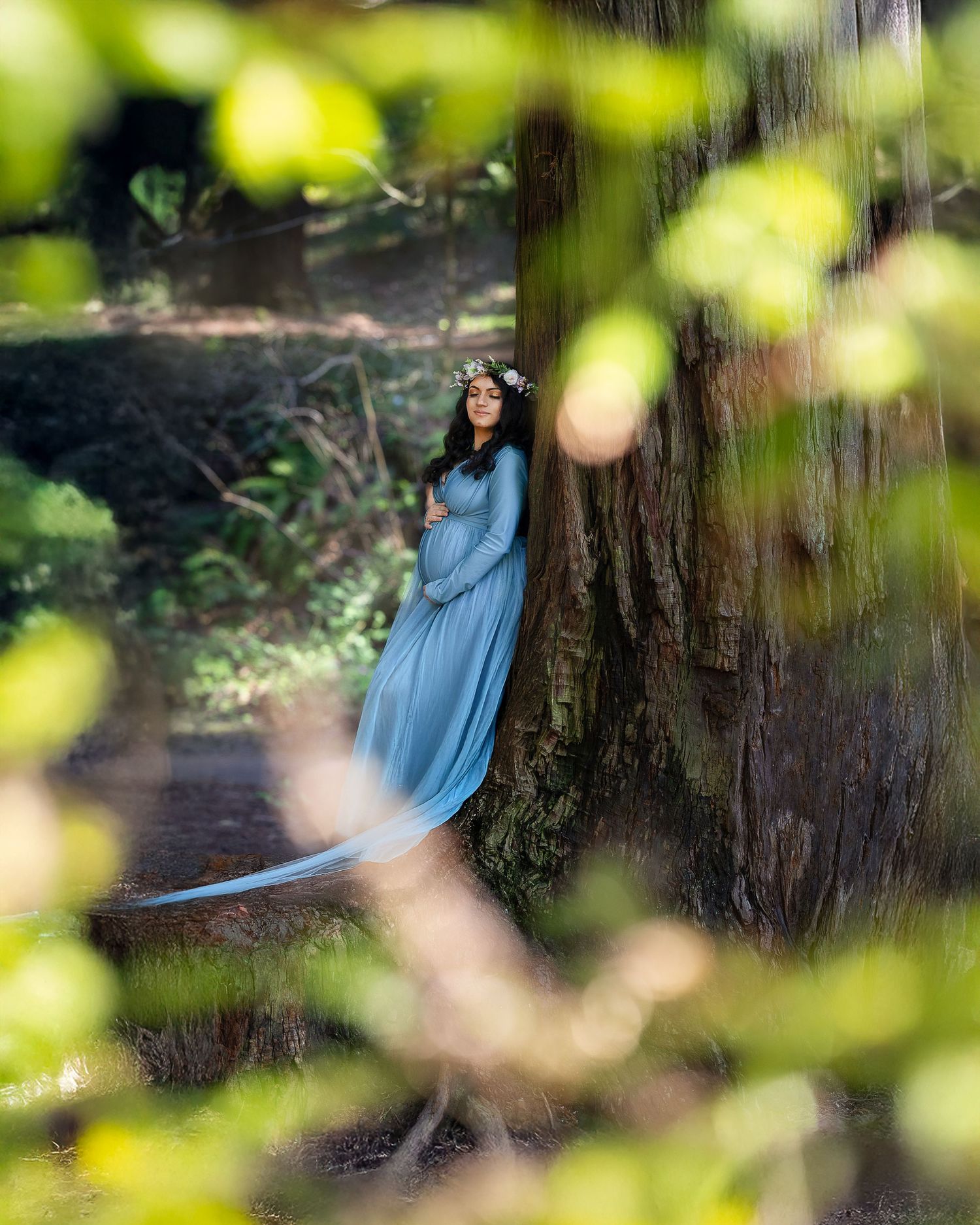 A figure in a flowing blue dress twirls gracefully among tall redwood trees in dappled sunlight.