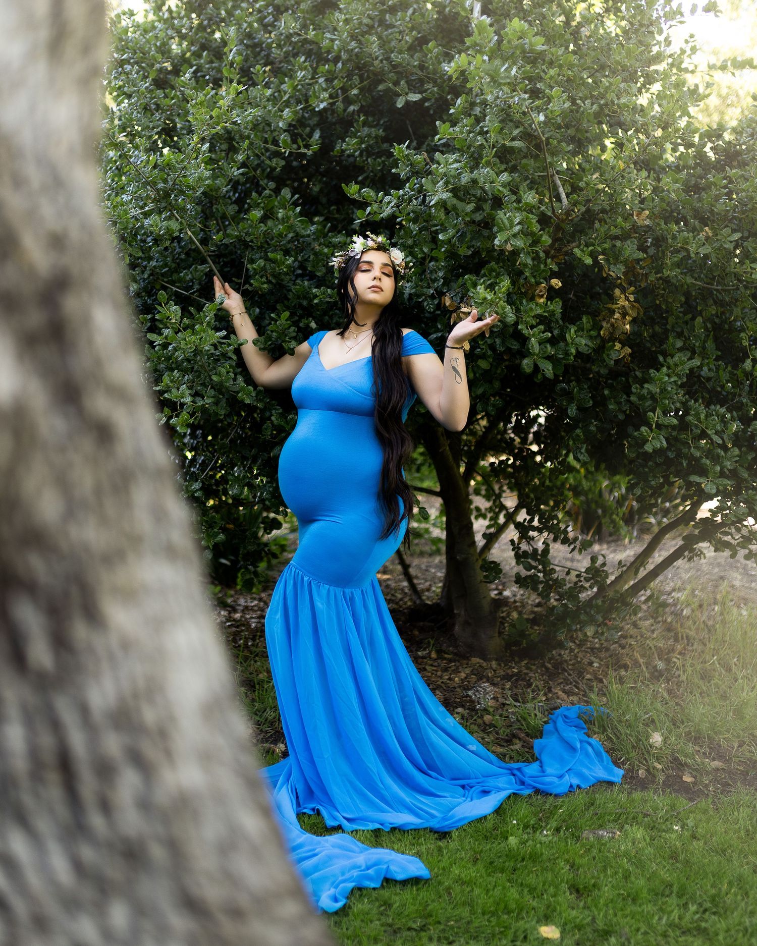 A flowing bright blue dress twirls gracefully in an outdoor garden setting with green foliage in the background.