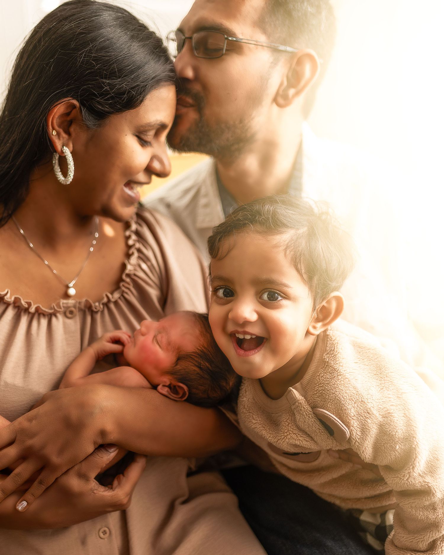 A loving family shares a tender moment together with their newborn baby in warm sunlit setting.