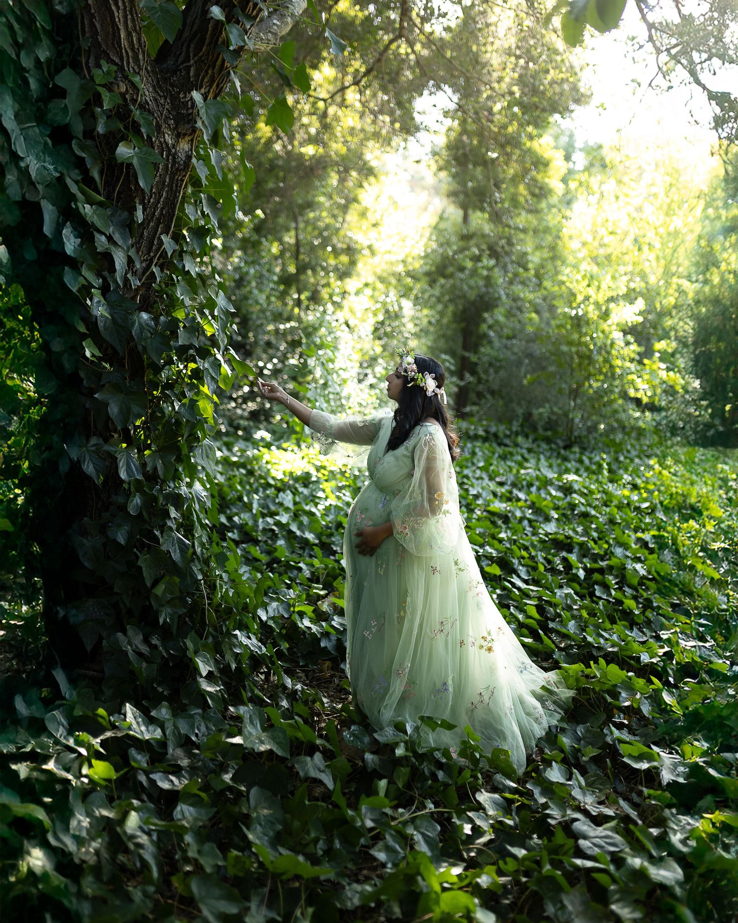 A figure in a flowing white dress moves gracefully through a lush green garden setting in dappled sunlight.
