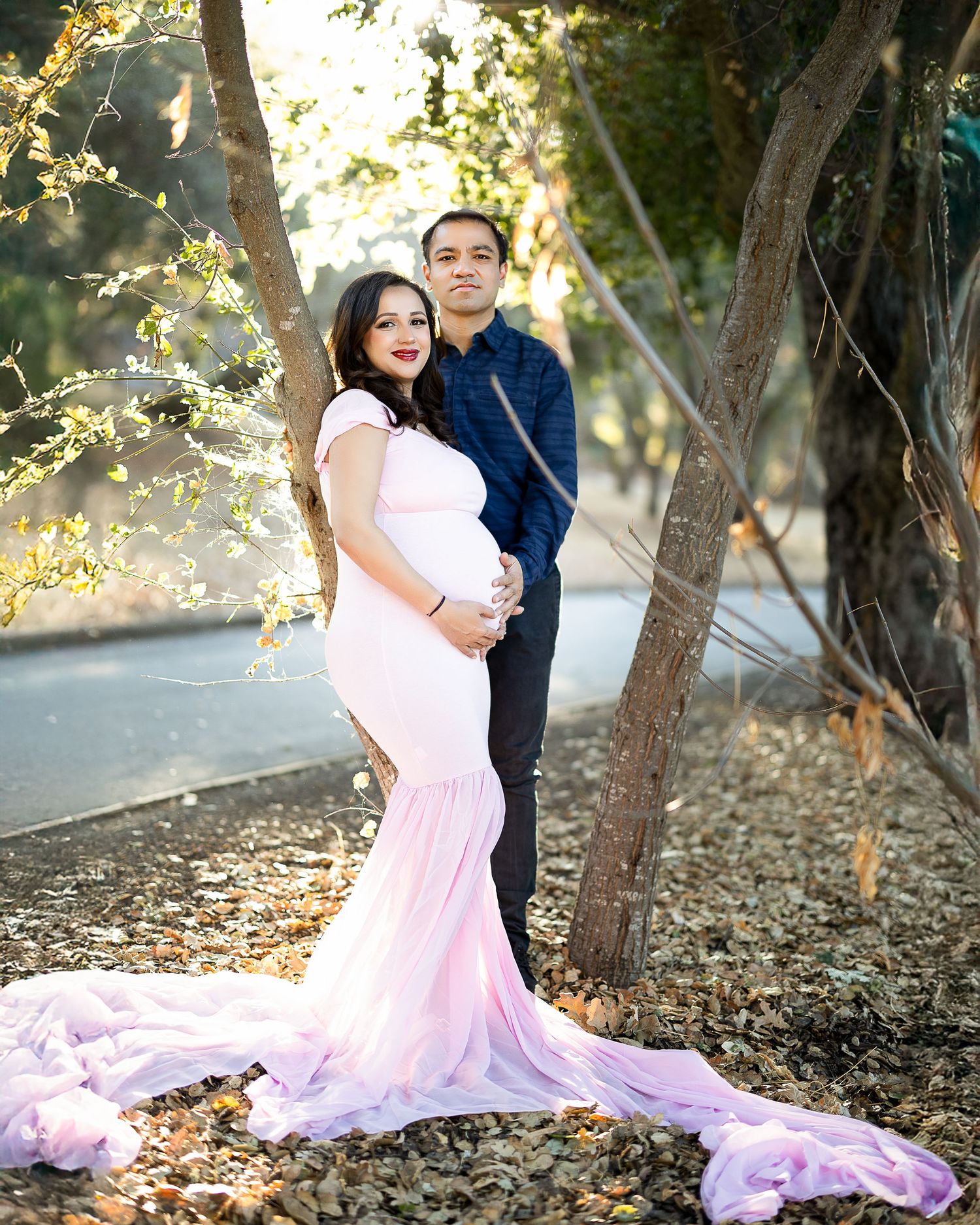 A romantic couple poses in a wooded area with a flowing pink dress creating an ethereal outdoor portrait.