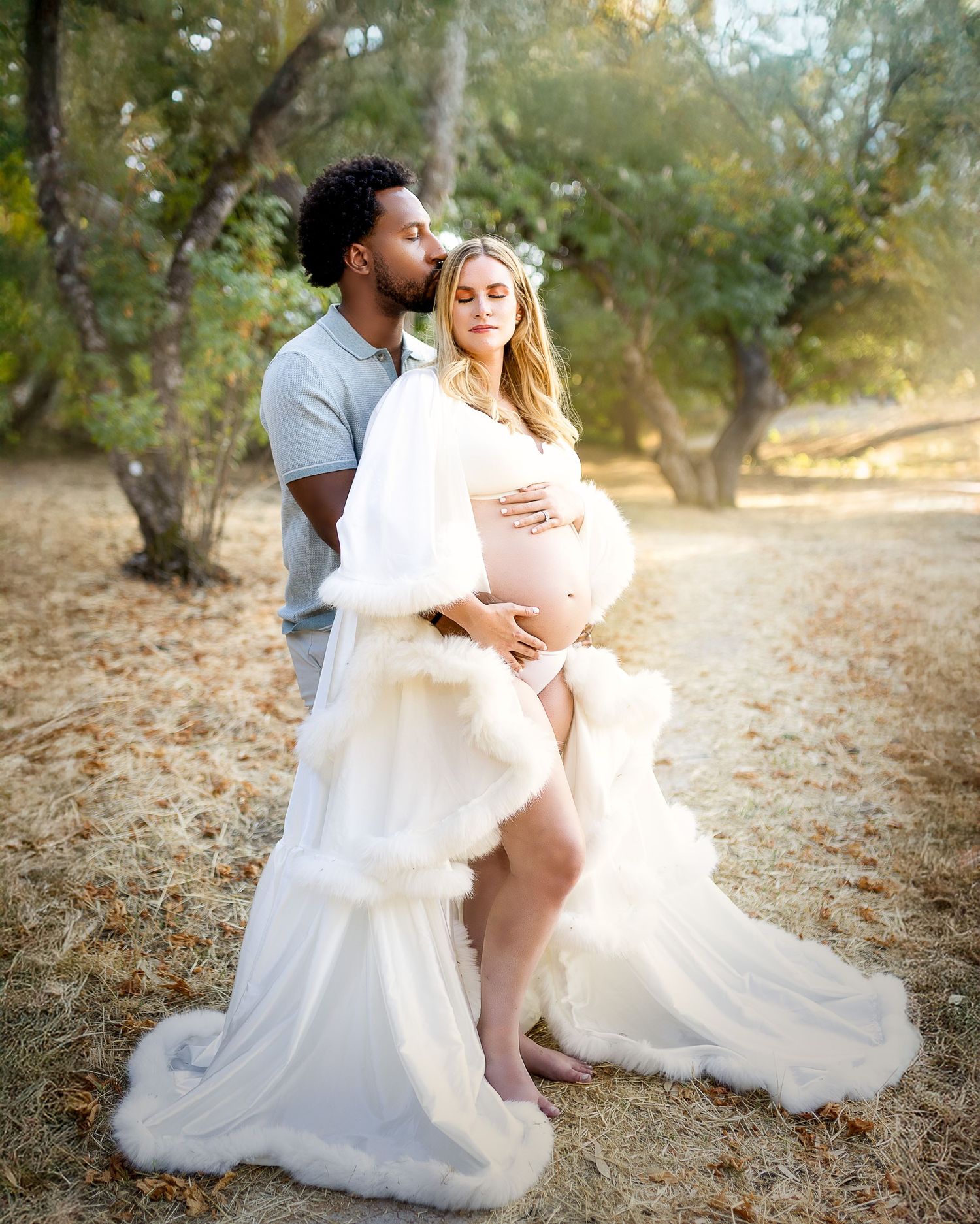 A romantic couple embraces on the ground during an outdoor photo session in a natural wooded setting.