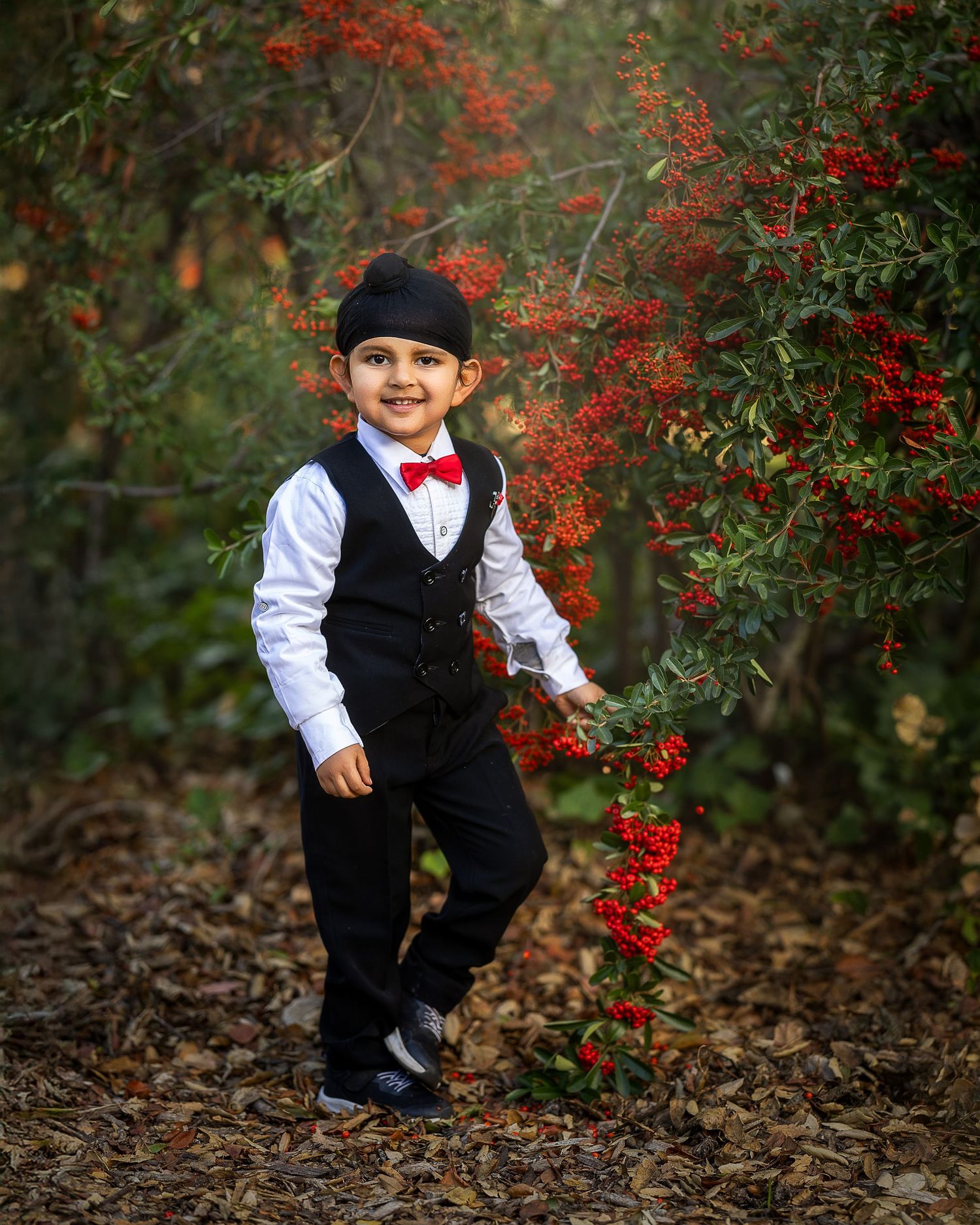 Formal black vest and red bowtie outfit photographed against vibrant red berries and green foliage in autumn setting.