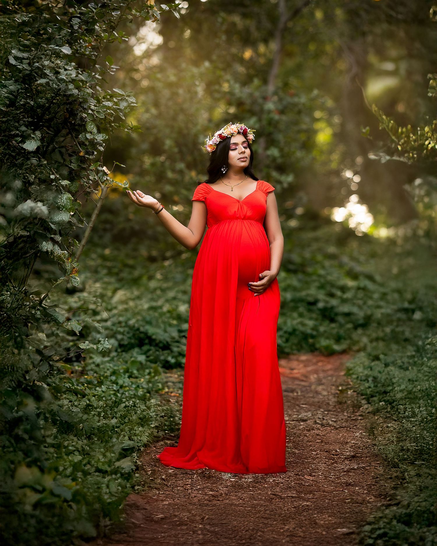 A figure in a flowing red dress stands on a wooded path during golden hour with sunlight filtering through trees.