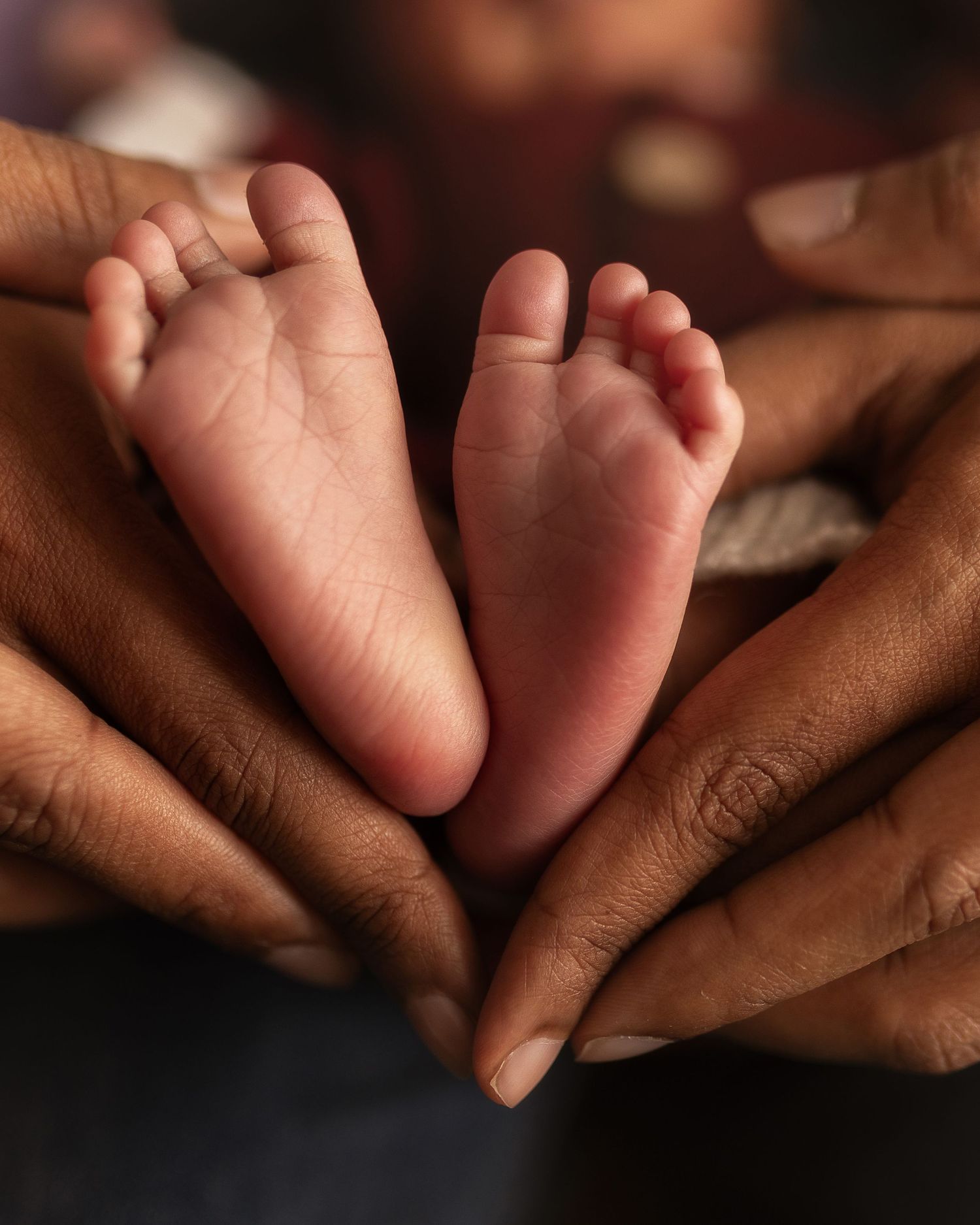 Close-up series of tiny newborn baby feet resting against dark brown skin in warm lighting.