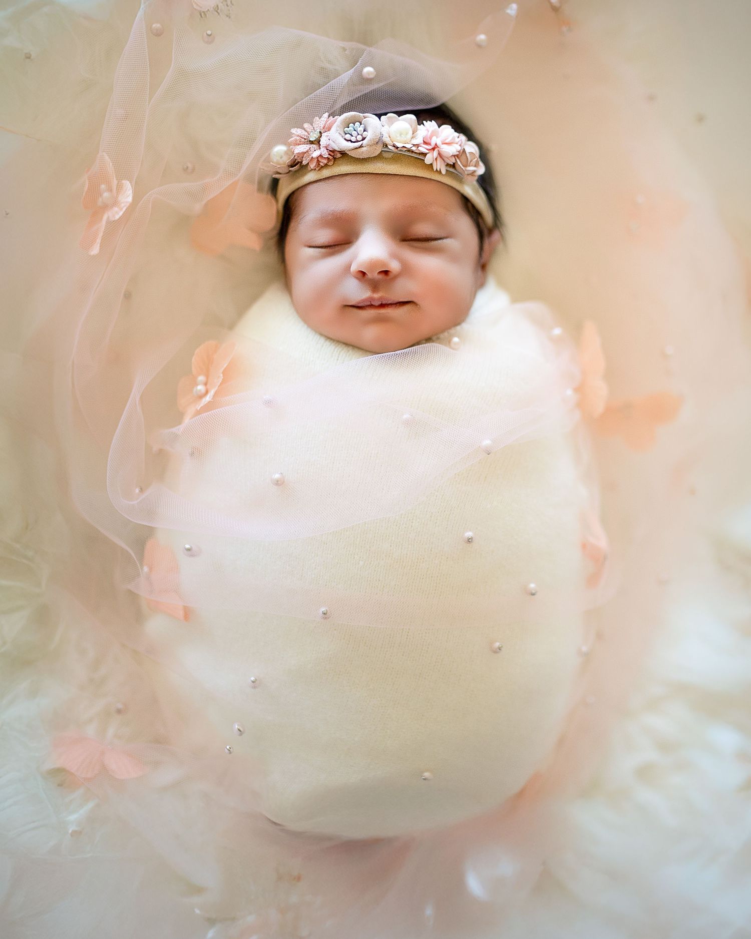A dreamy newborn photography series showing a sleeping baby in soft, ethereal lighting with peachy tones and white fabric.