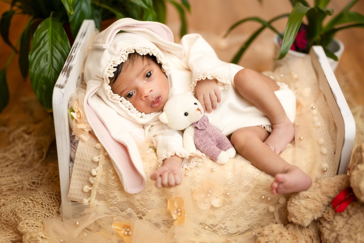 A sleeping baby wearing a pink outfit lies peacefully in a cozy blanket with stuffed animals nearby.