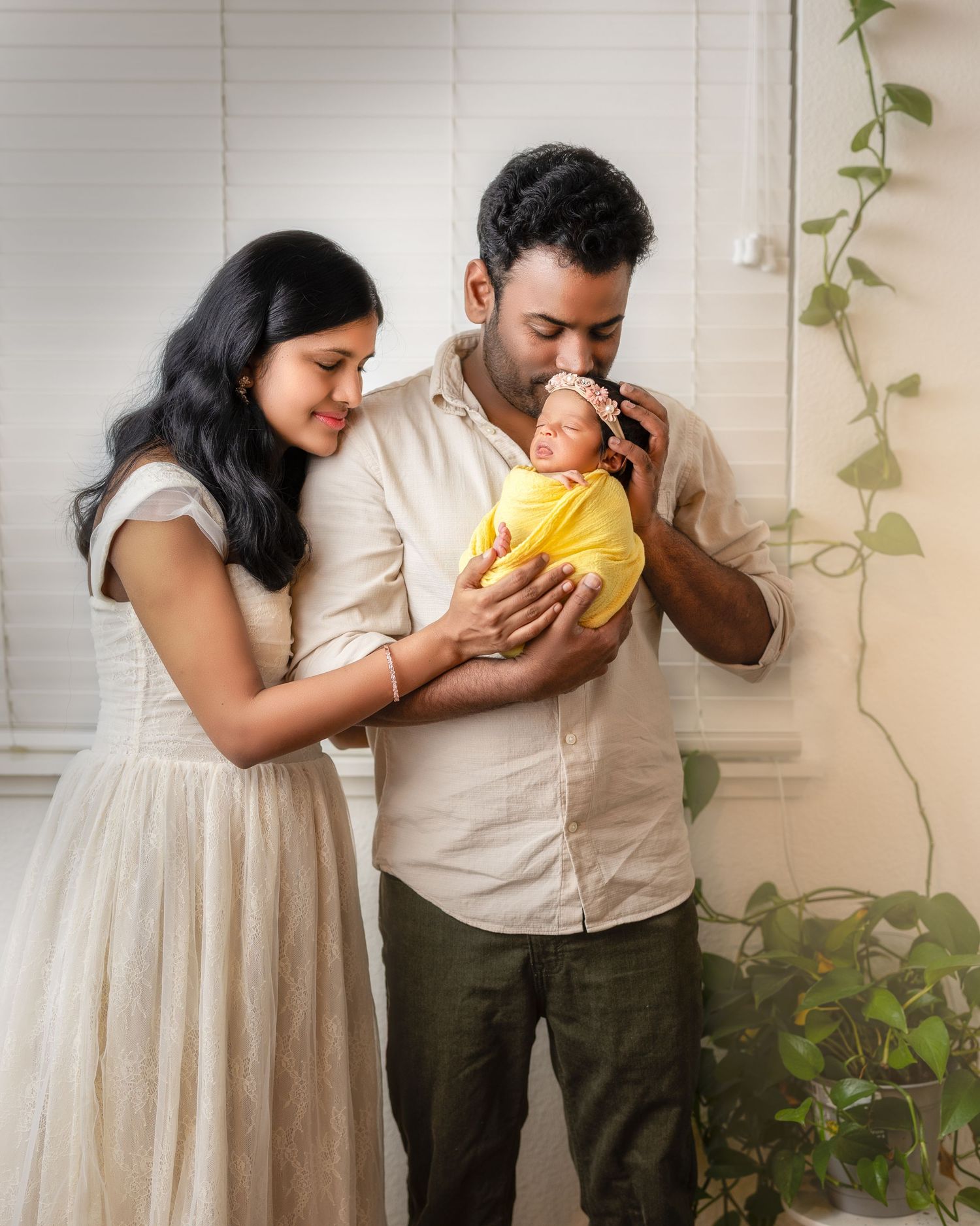 A couple in white and olive clothing share a large yellow fruit while standing against a white brick wall with climbing vines.