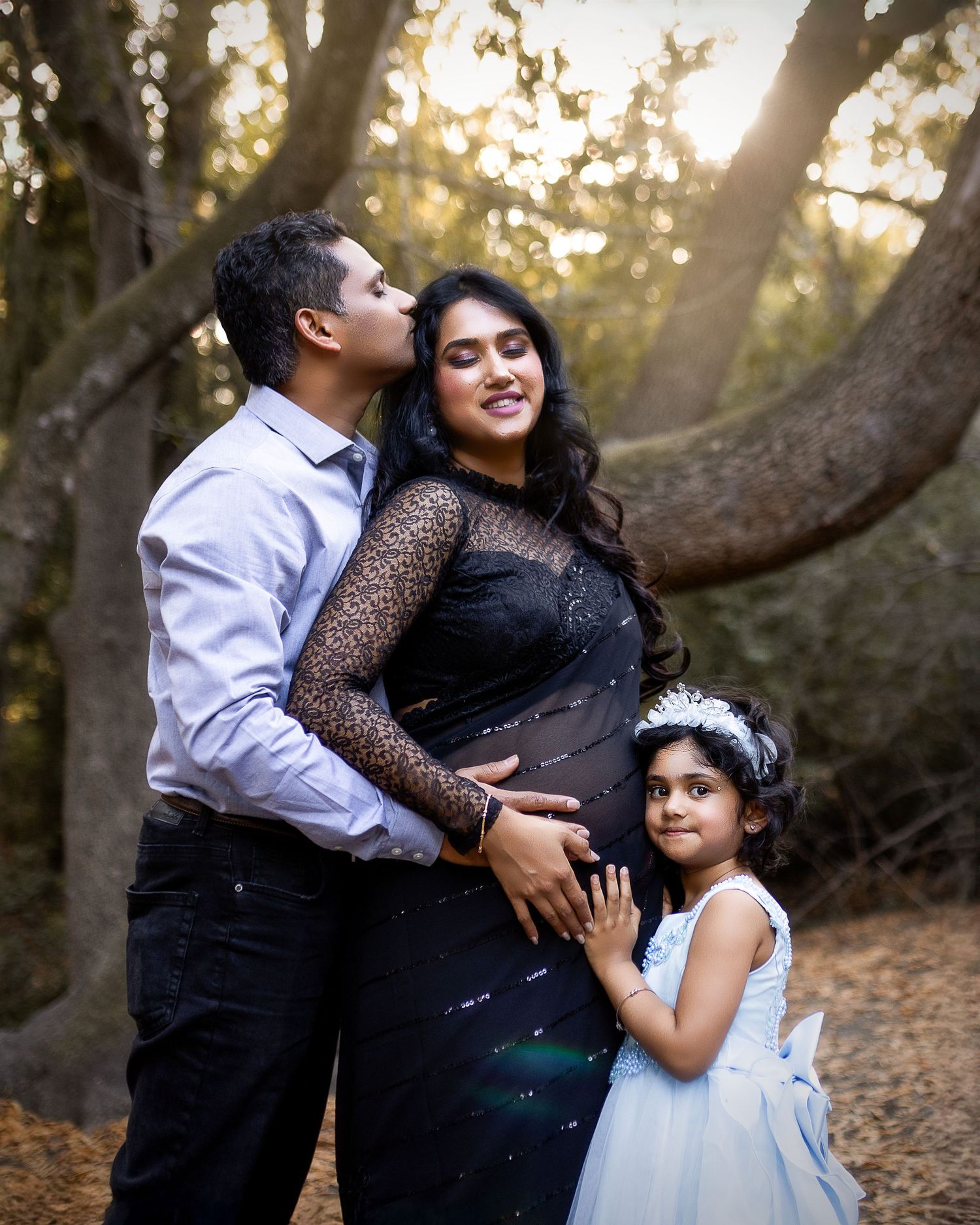 A family embraces in a tender moment during a golden sunset photoshoot in a wooded outdoor setting.