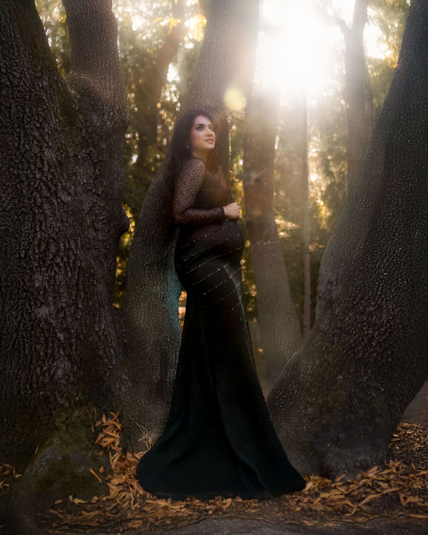 A figure in a flowing black dress stands mysteriously among sunlit trees in a misty forest setting.