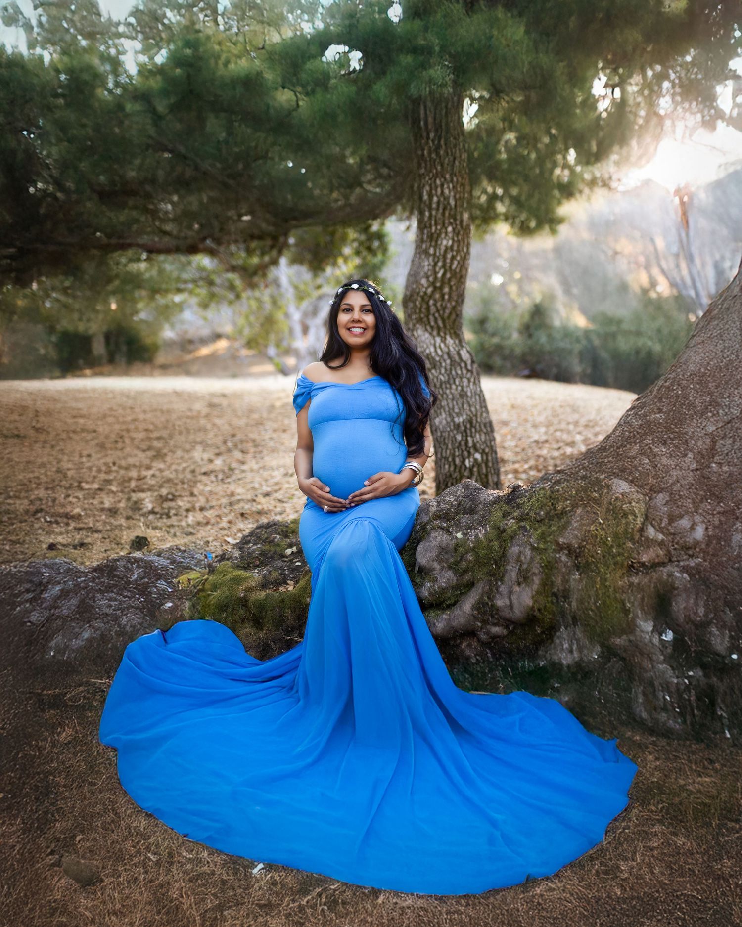 A flowing royal blue dress creates a dramatic silhouette against a rustic woodland setting during a photo session.