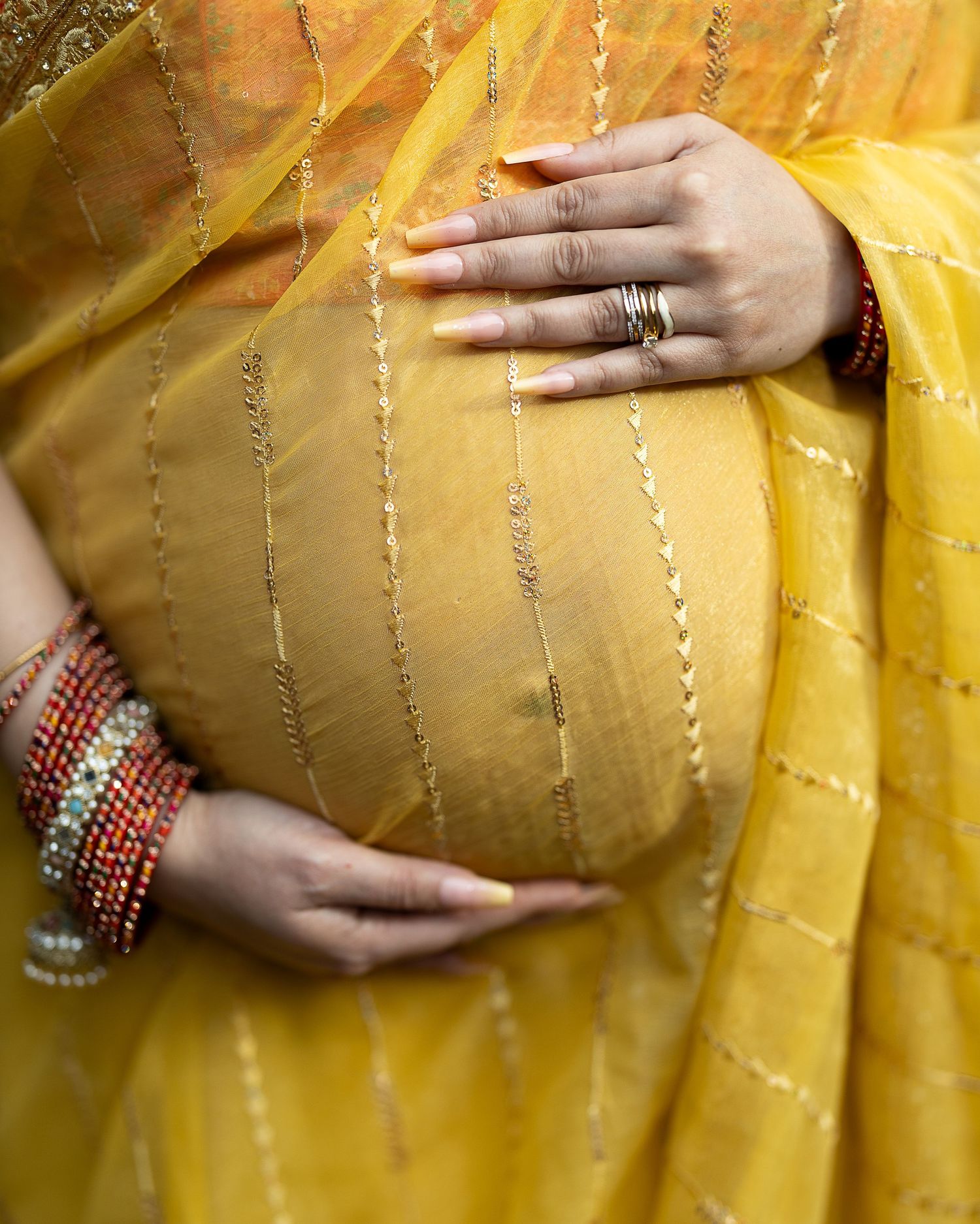 A hand adorned with bangles rests on a yellow embroidered fabric with delicate silver threading details.