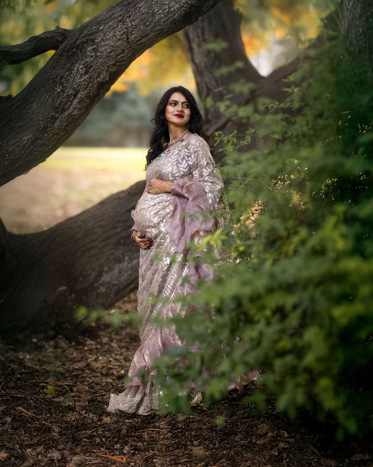 A figure in a flowing pink dress poses gracefully against a backdrop of trees and dappled sunlight in a forest setting.