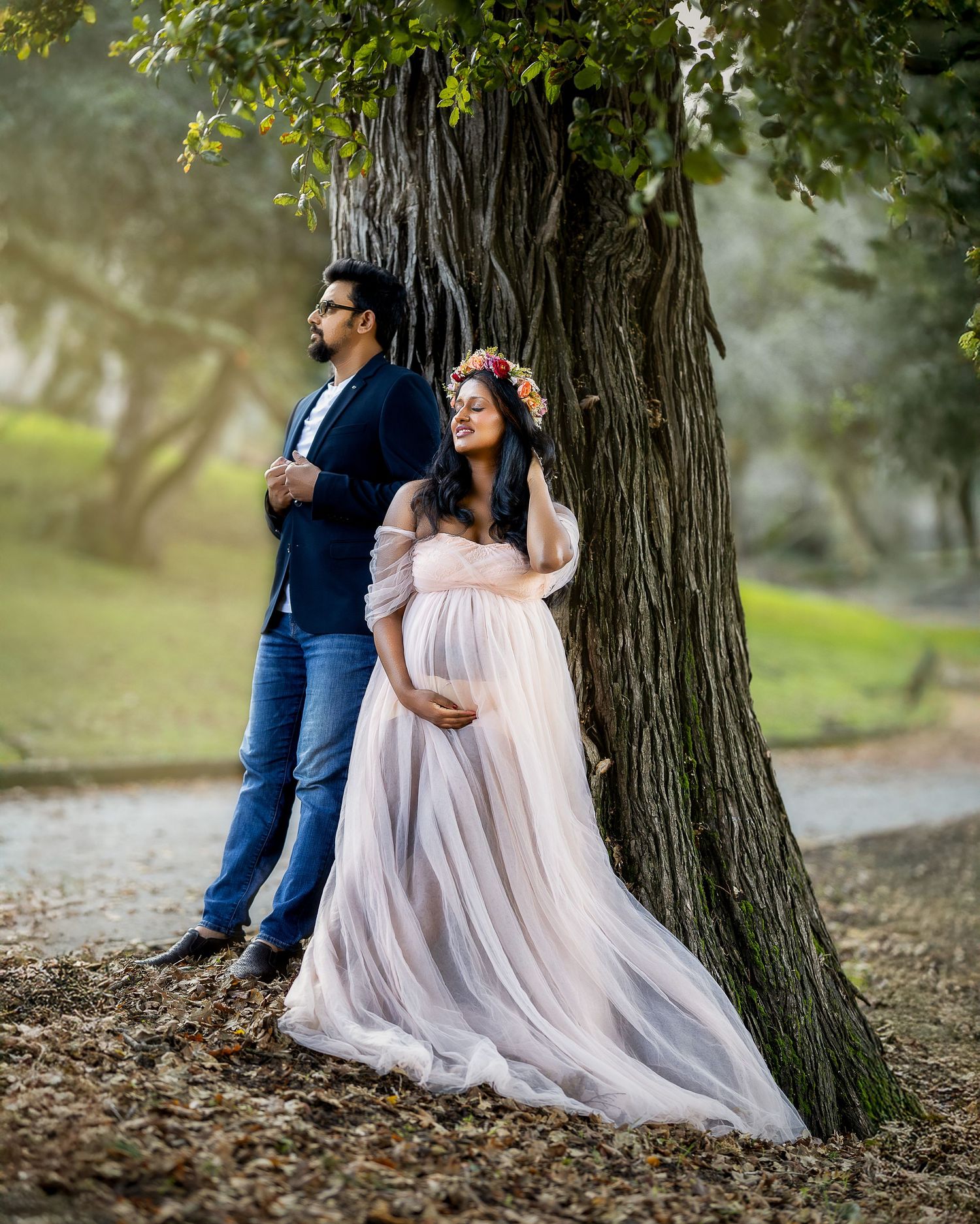 A couple in romantic poses against a large tree trunk in a dreamy outdoor setting with soft lighting and autumn leaves.