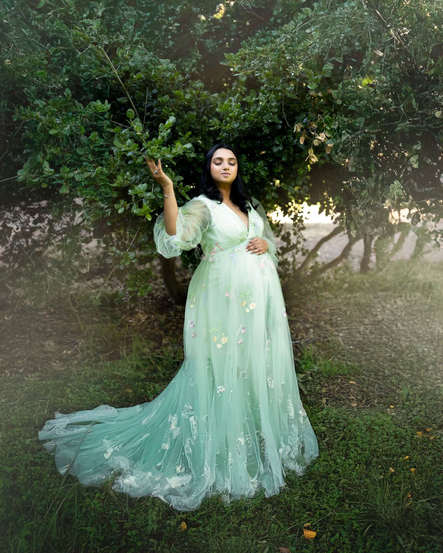 A dreamy portrait in a mint green tulle gown with flowing fabric and floral details in an enchanted garden setting.