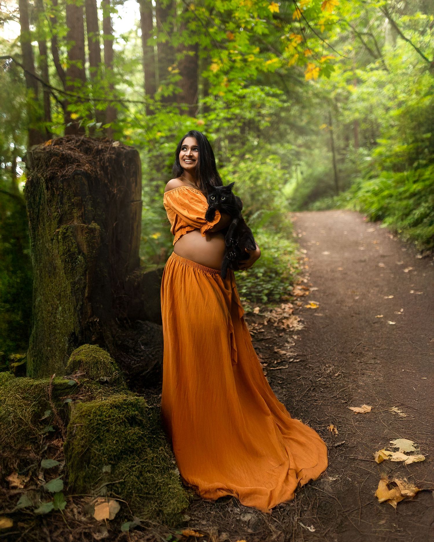 A person in a flowing burnt orange dress walks along a misty forest path surrounded by green trees and fallen leaves.