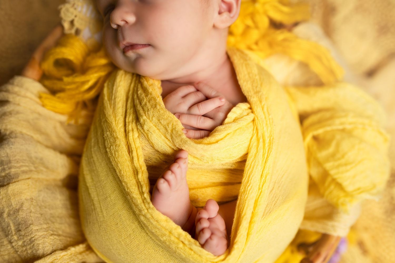 A sleeping newborn baby wrapped in soft yellow fabric lying on a white blanket.