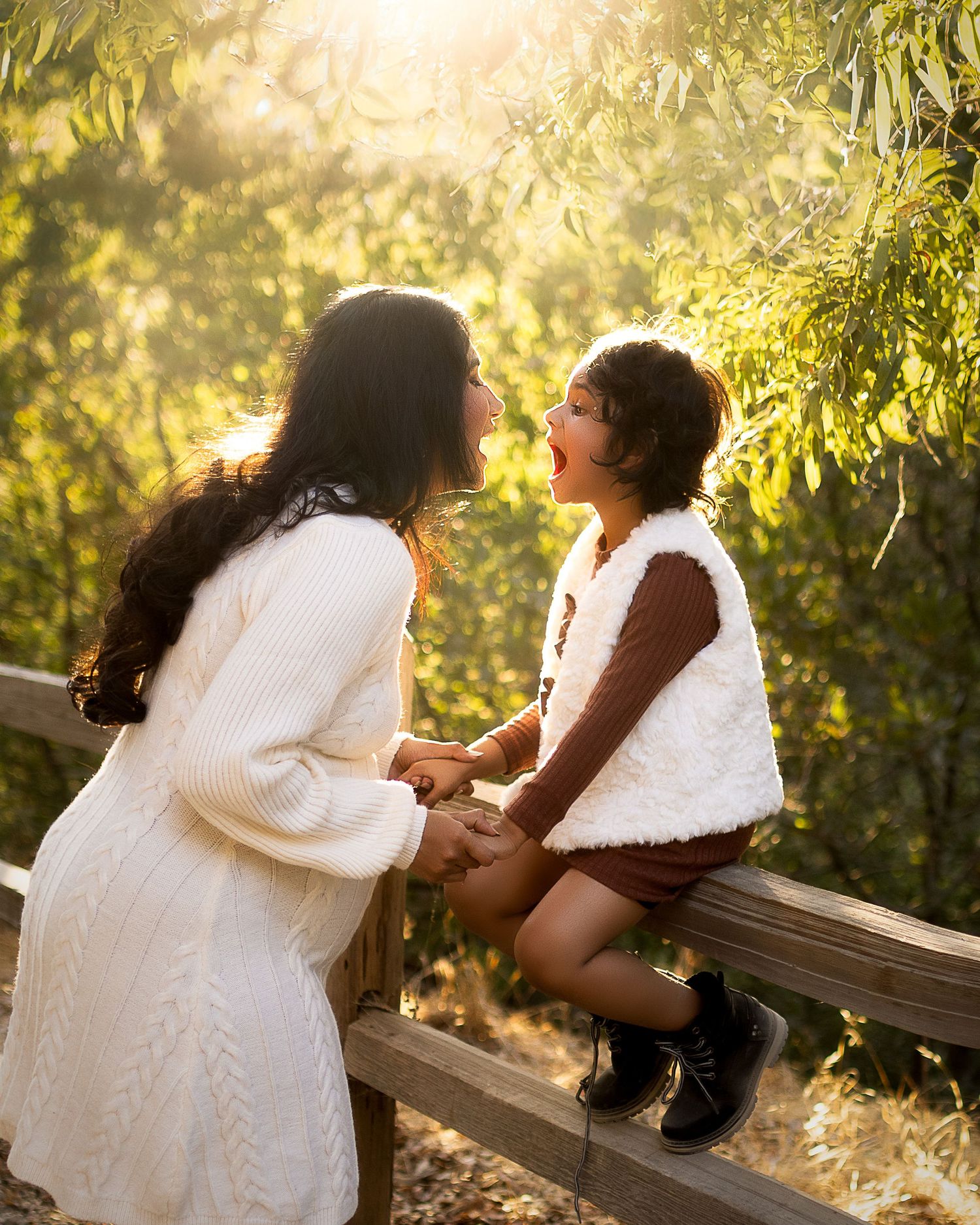 A couple in white outfits share a tender moment on a wooden bench at sunset in a natural outdoor setting.