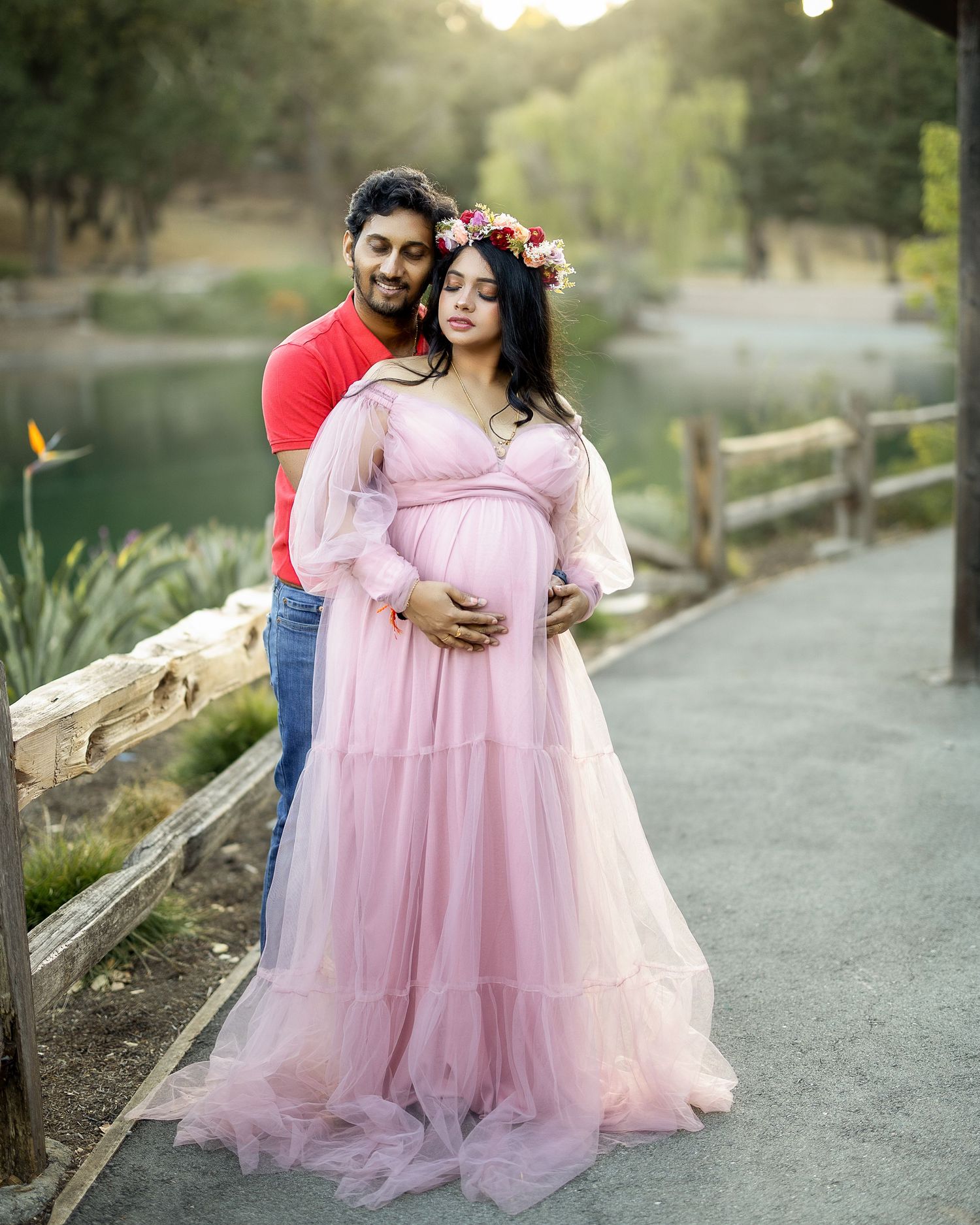A couple in matching pink attire poses together on a winding path during a golden hour photoshoot.